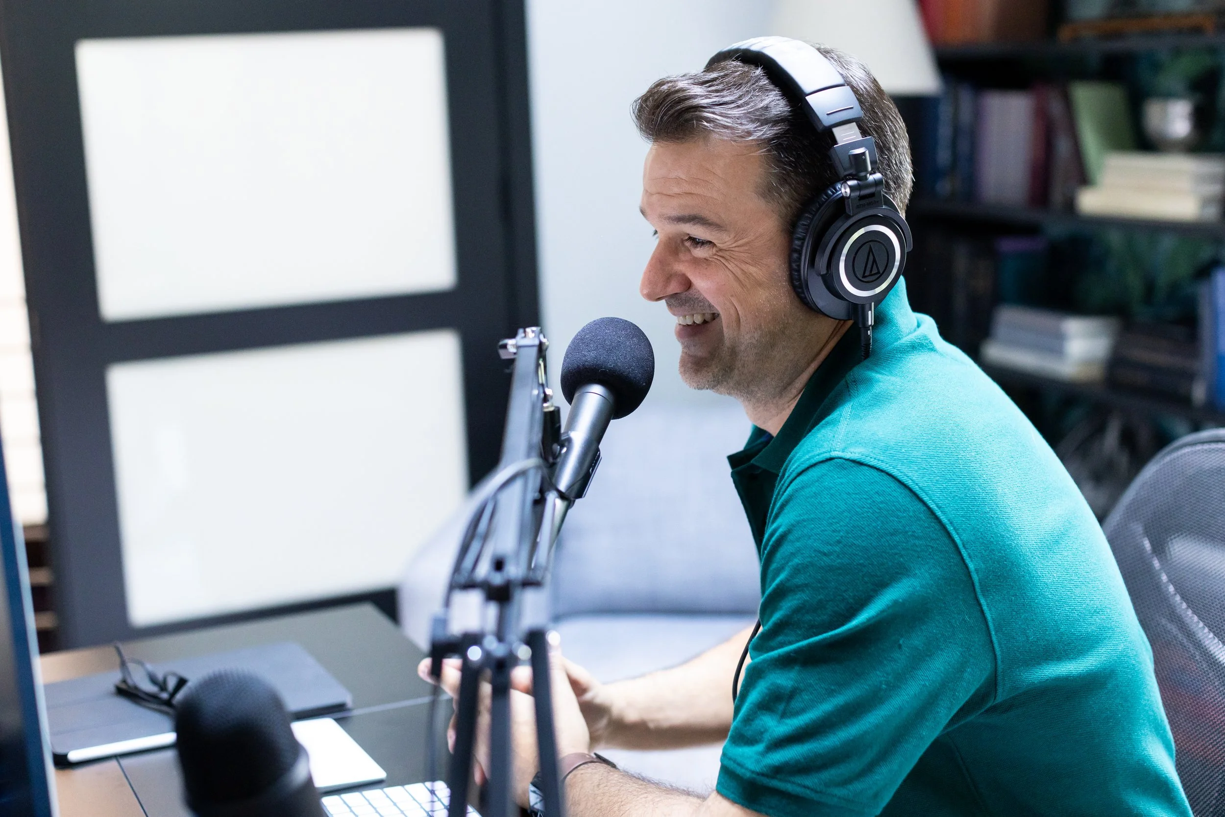 Lance Pendleton, with headphones, sitting in front of a microphone in a podcast studio, smiling while recording.