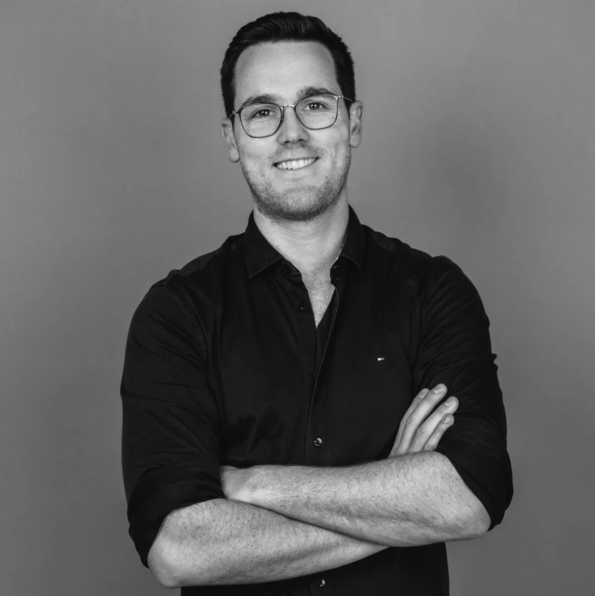 Picture of white male in a black top with glasses, smiling.