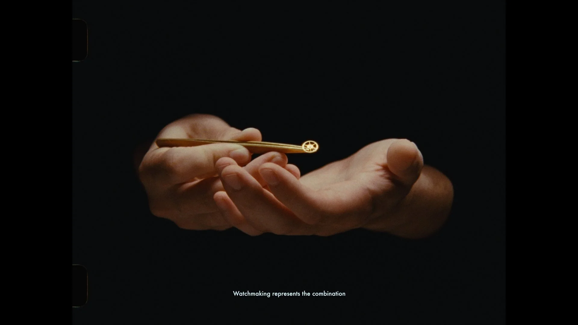 Close-up of a hand holding a golden object with a small wheel on one end, against a dark background. Subtitle reads, "Watchmaking represents the combination."
