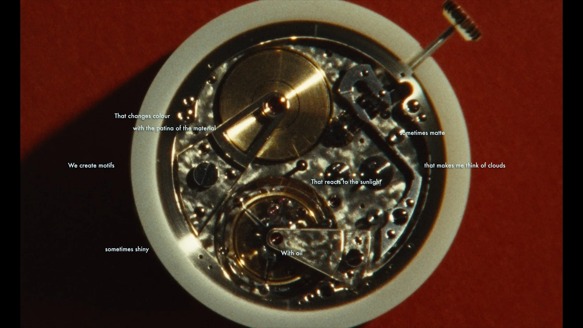 Close-up of a watch mechanism with several gears, screws, and metal parts. Overlayed text describes the process of creating motifs through material's patina, which reacts to sunlight and oil, changing color, sometimes matte or shiny.
