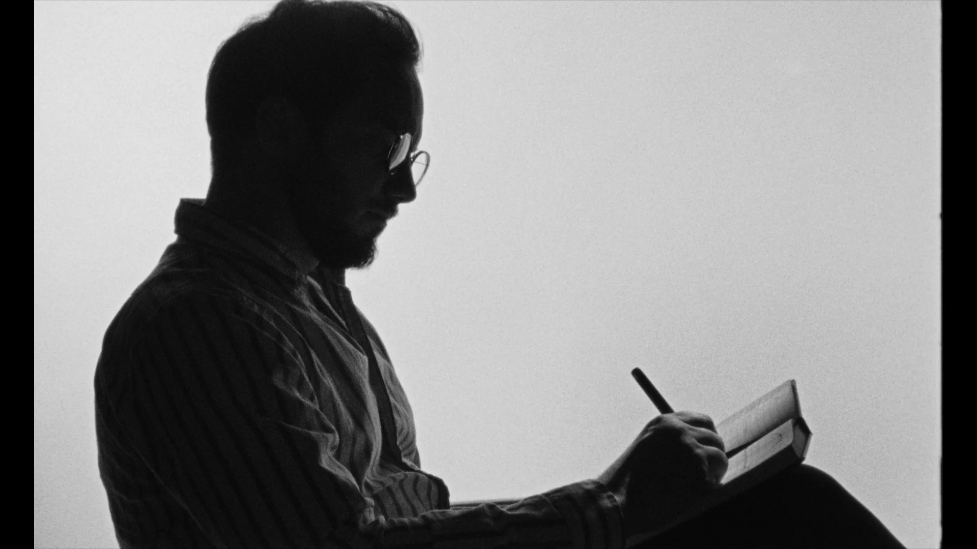 Silhouette of a man with glasses, writing in a notebook. Black and white photo.