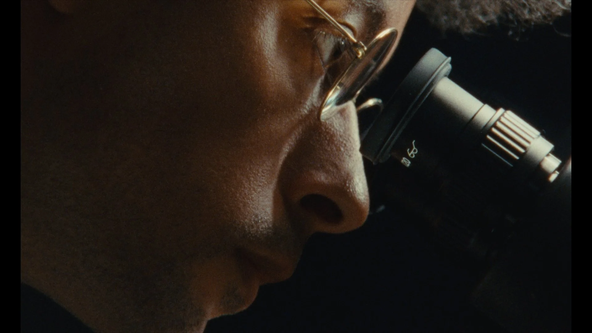Close-up of a person looking through a microscope, focusing on their face and the microscope's lens.
