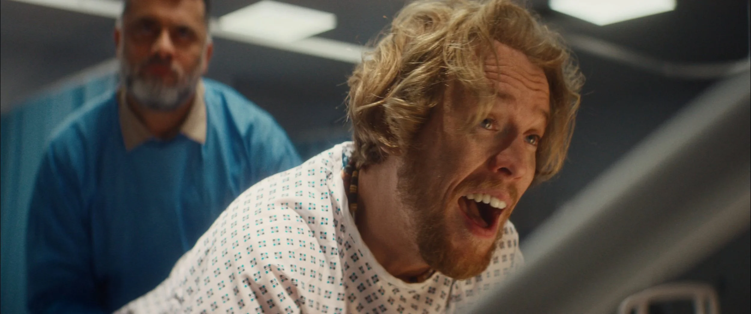 Two men in hospital gowns and scrubs are in a medical setting, appearing distressed or excited.