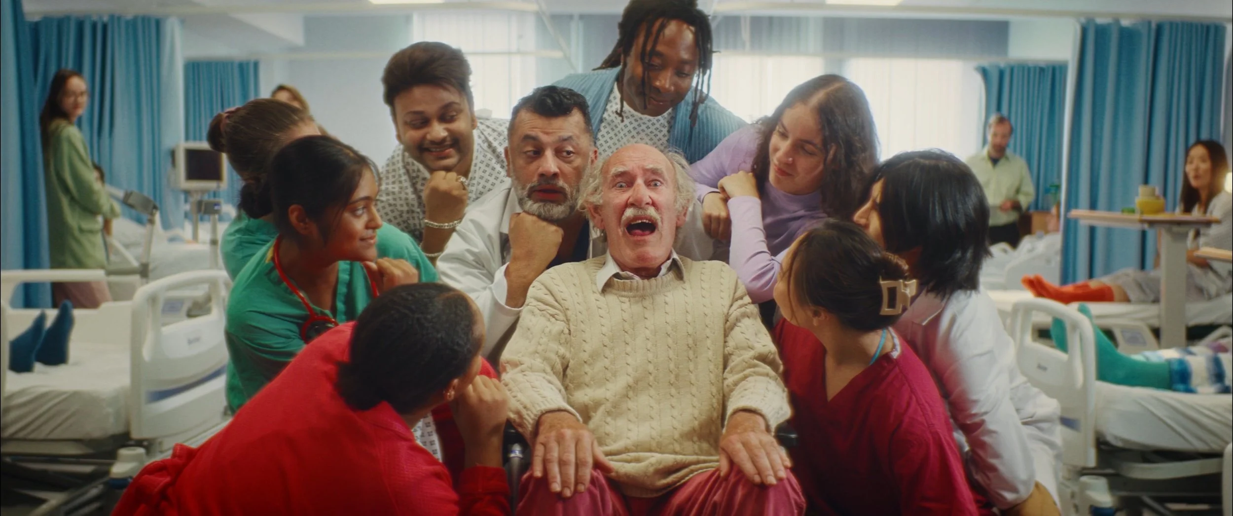 A diverse group of healthcare workers and patients surrounding an elderly man in a hospital room, displaying a mix of surprised and amused expressions.
