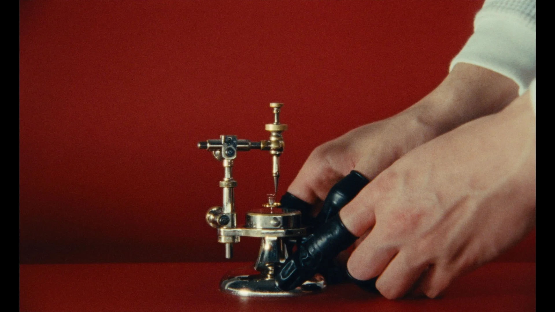 Close-up of a person's hand operating a vintage brass micromanipulator with a sharp probe attached, set against a red background.