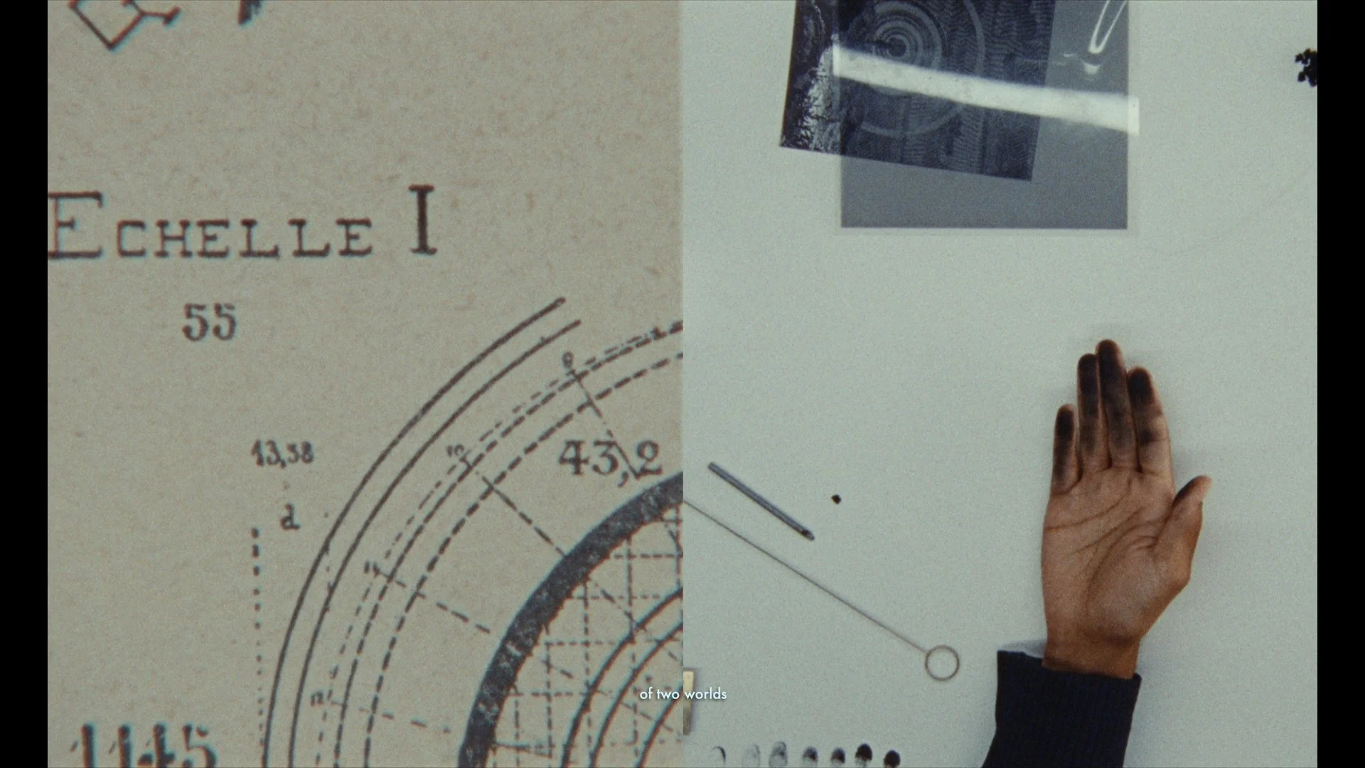 Close-up of a technical drawing or blueprint, with text reading 'Echelle 1' and numbers such as '55', '43.9', and '13.38'. A hand is visible on the right side touching the surface, suggesting interaction with the drawing.