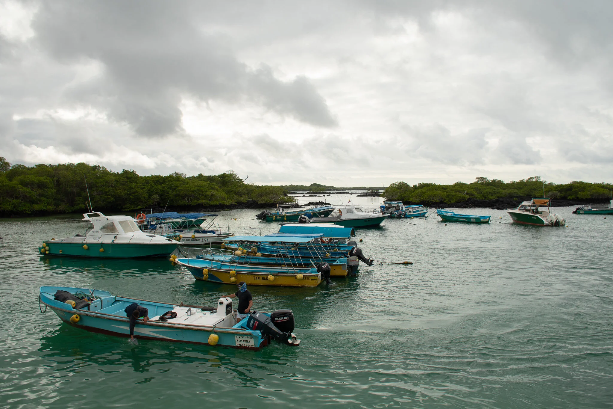 Multiple blue boats floating in the ocean in the Galapagos with a cloudy sky in the background.