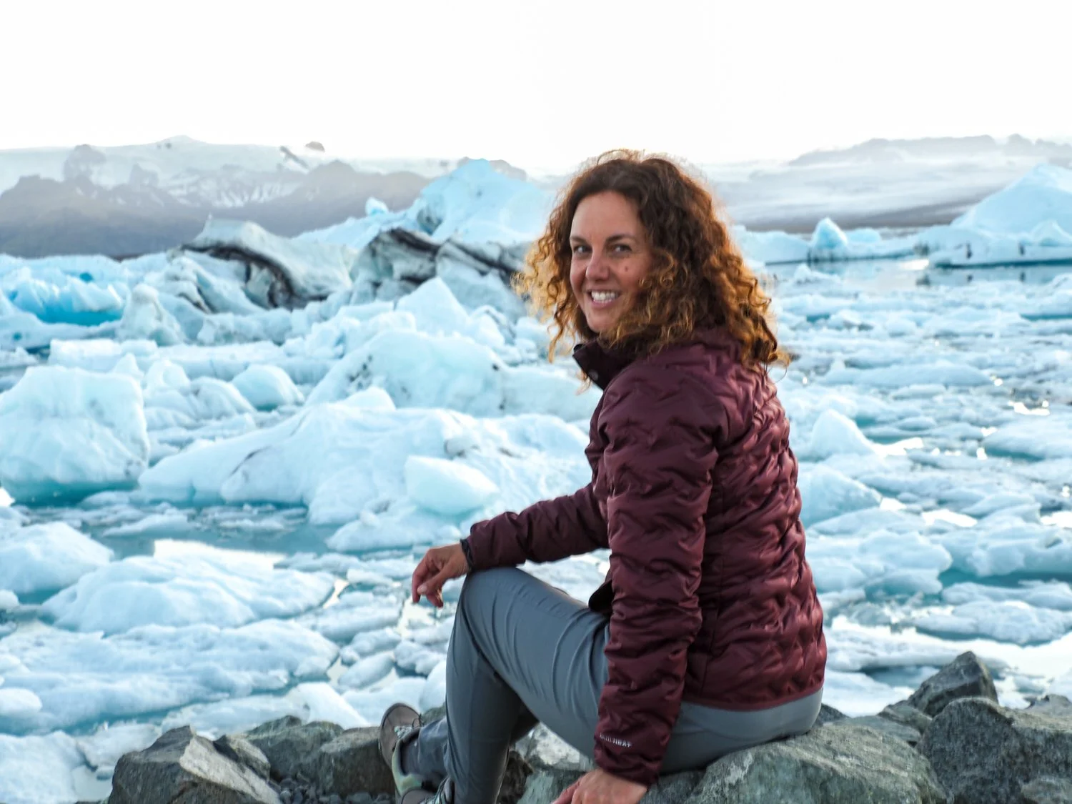 In Iceland, Juli is sitting on a rock and behind her is Glacier Lagoon