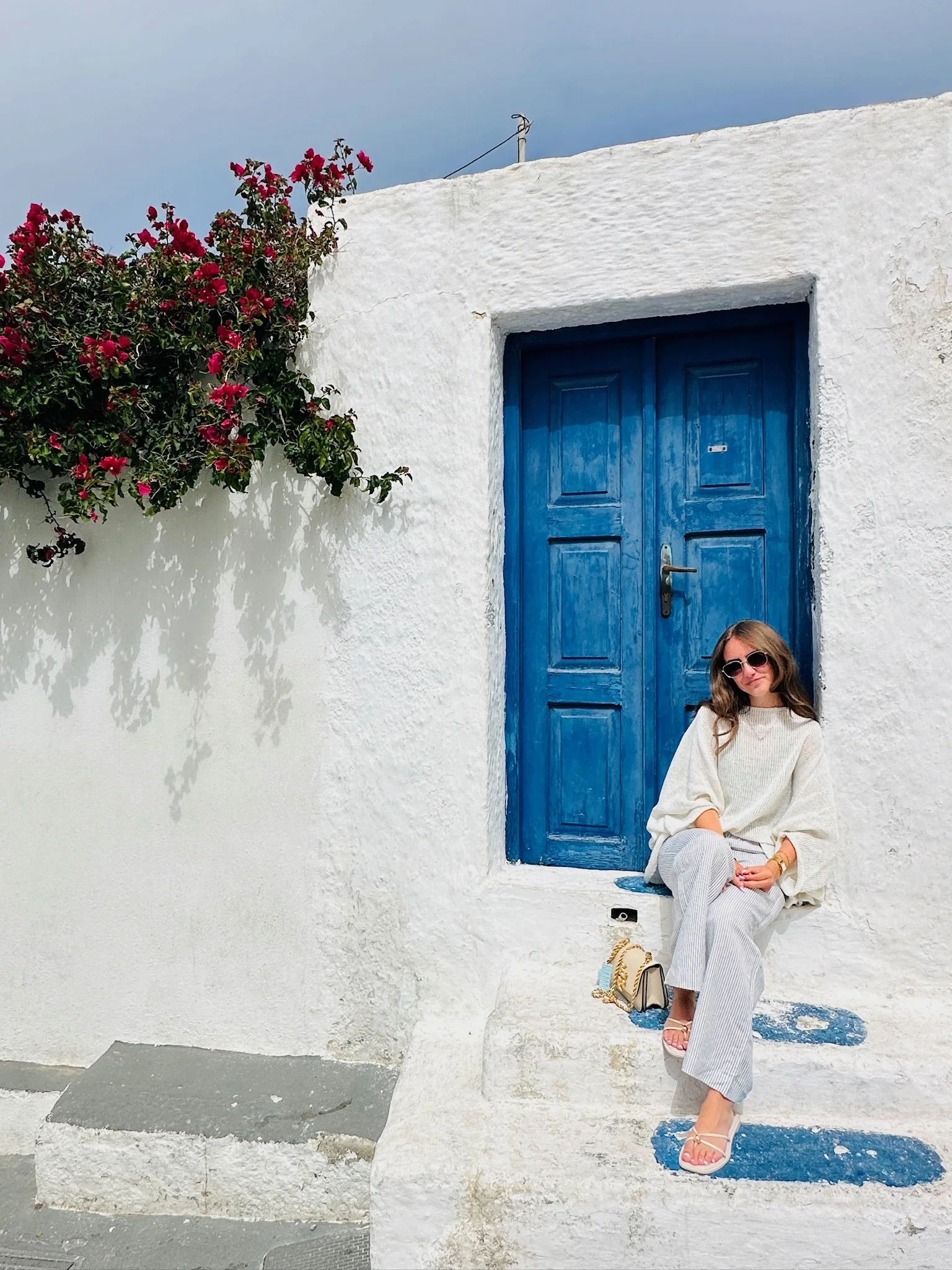 Young adult sitting at a blue doorstep in Santorini Greece