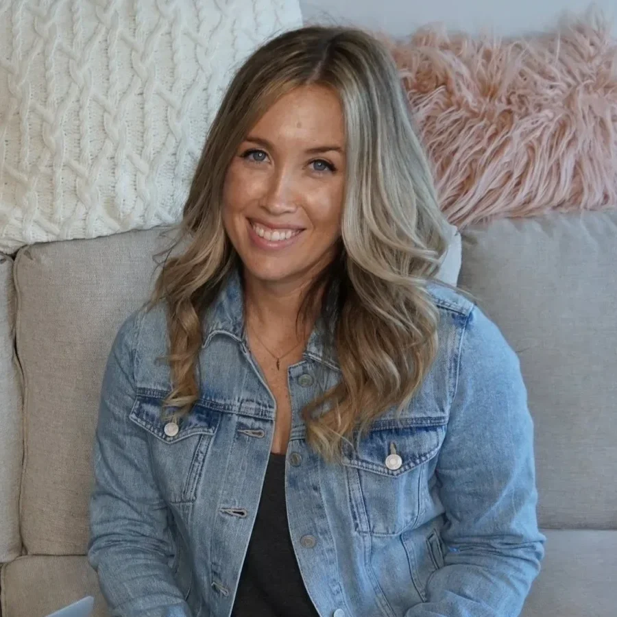 A woman with long blonde hair smiling while sitting on a beige couch with textured pillows in the background.