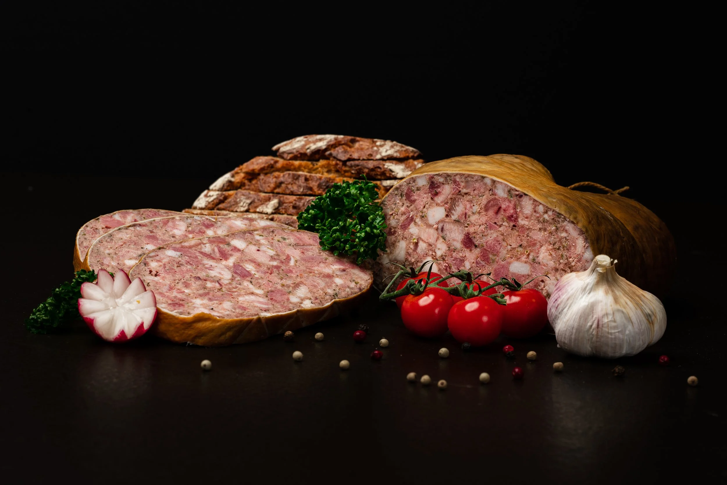 Aufschnitt, Tomaten, Knoblauch und Gewürze auf schwarzem Hintergrund.