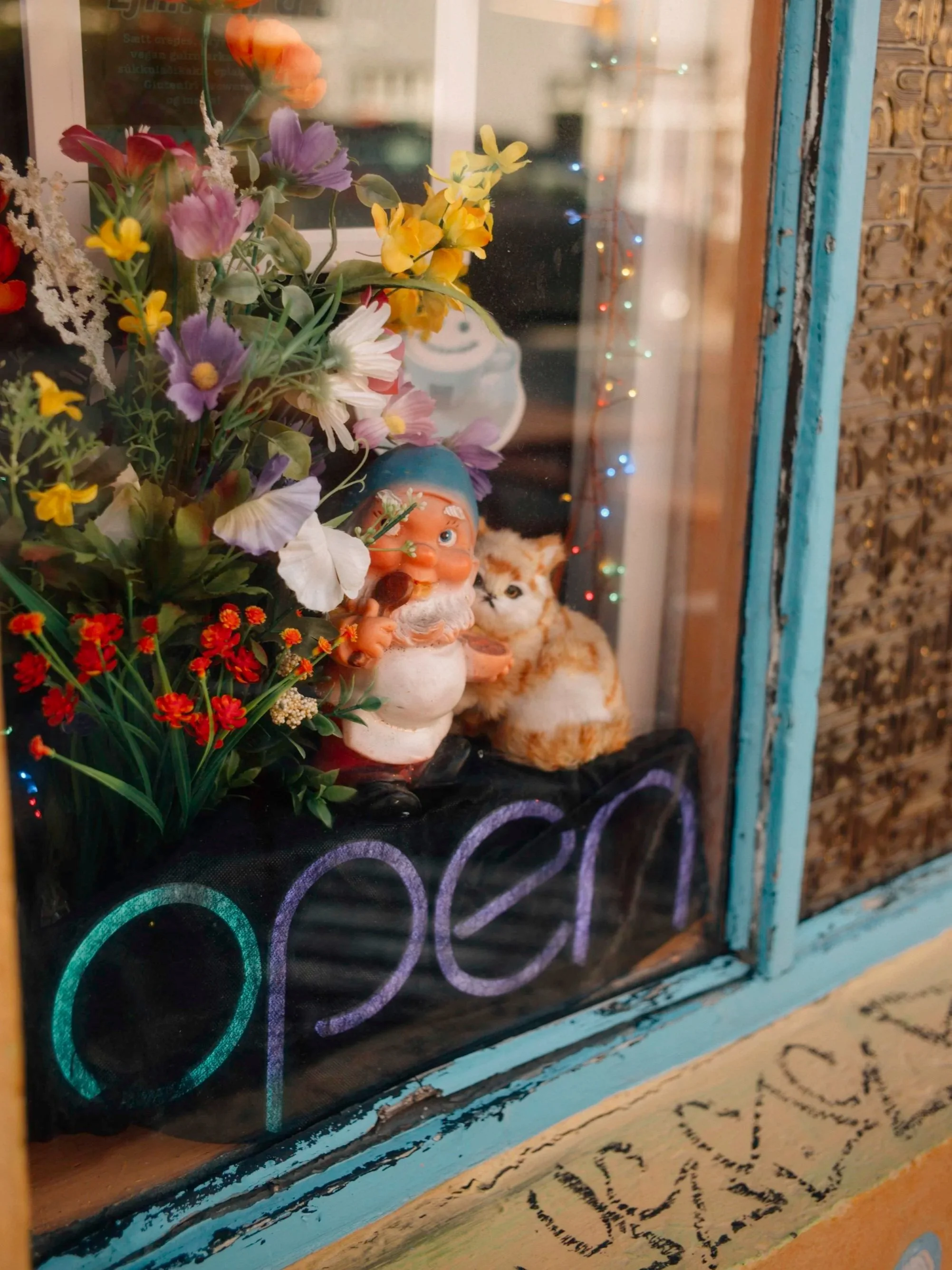 Blumenstrauß, Gartenzwerg und Katzefigur im Schaufenster eines Ladens mit leuchtenden Lichtern.