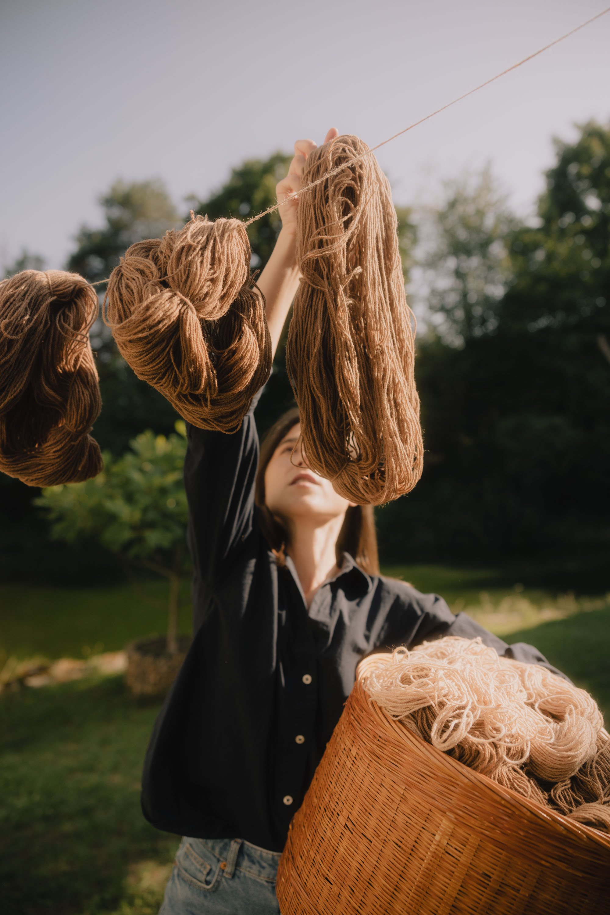 Frau hängt Strickwolle an einem Seil im Freien auf, mit einem Korb voller Strickwolle in ihrer Hand.