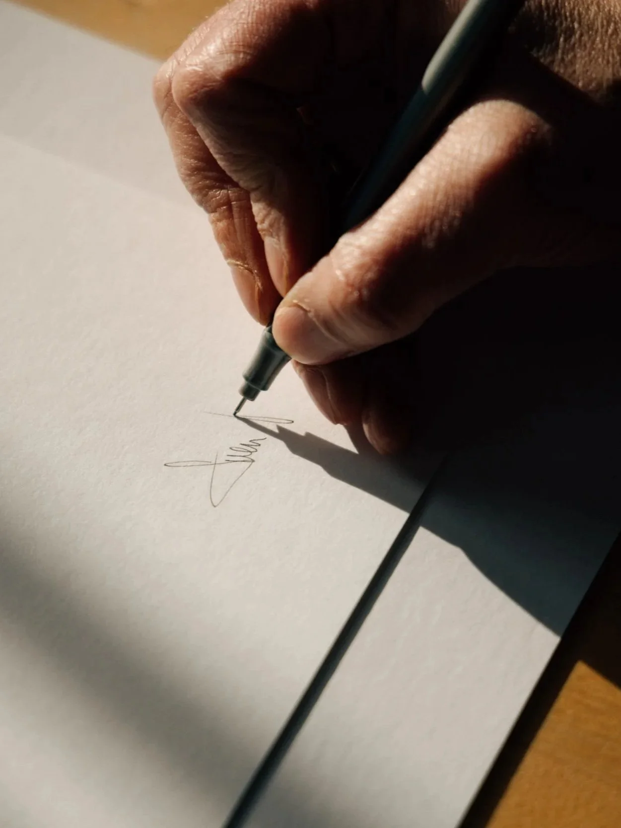 Nahaufnahme einer Hand, die mit einem schwarzen Füllfederhalter auf weißem Papier unterschreibt.