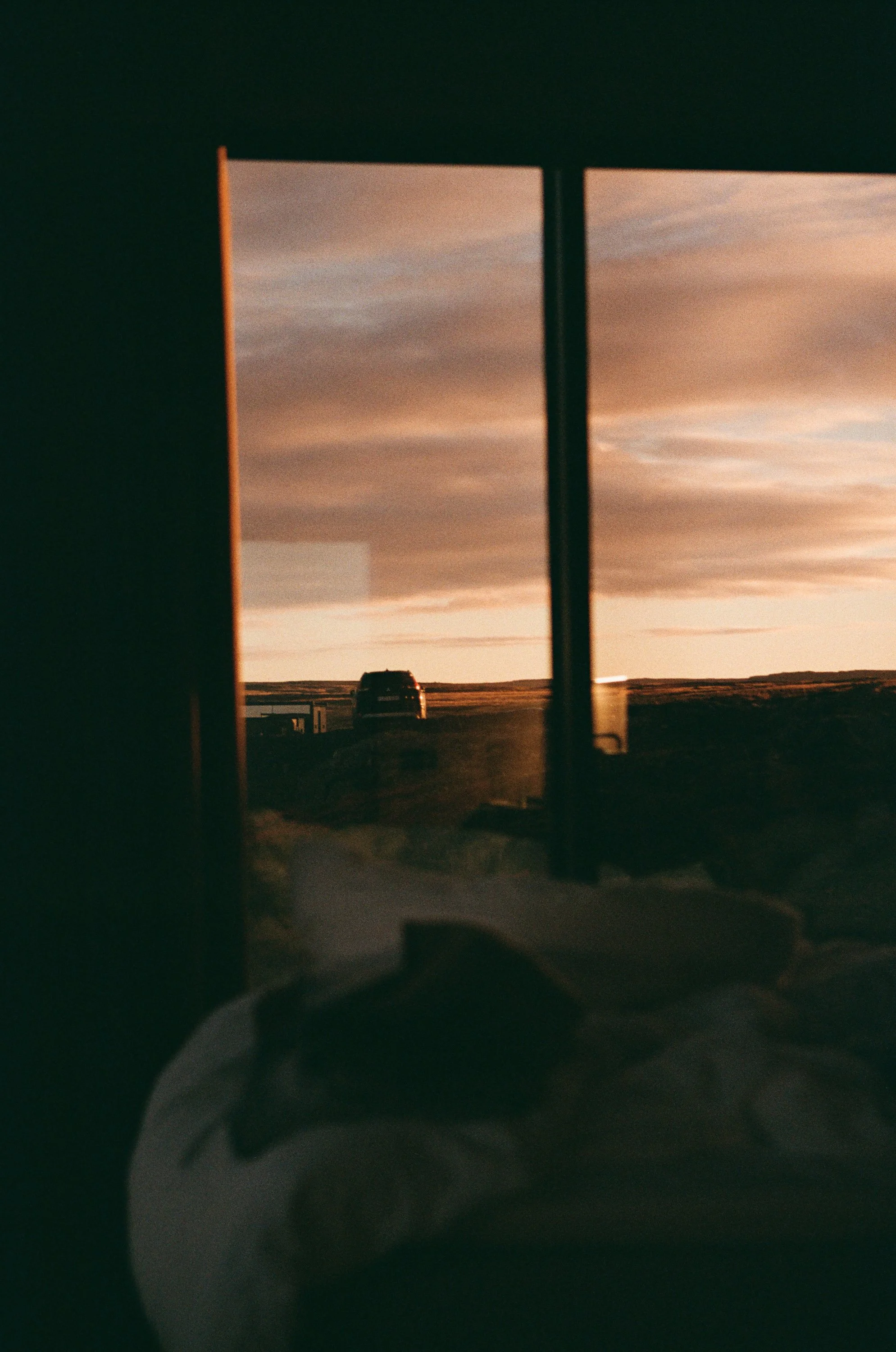 Blick durch ein Fenster auf eine Straße mit einem Auto bei Sonnenuntergang, reflektiert auf der Scheibe.