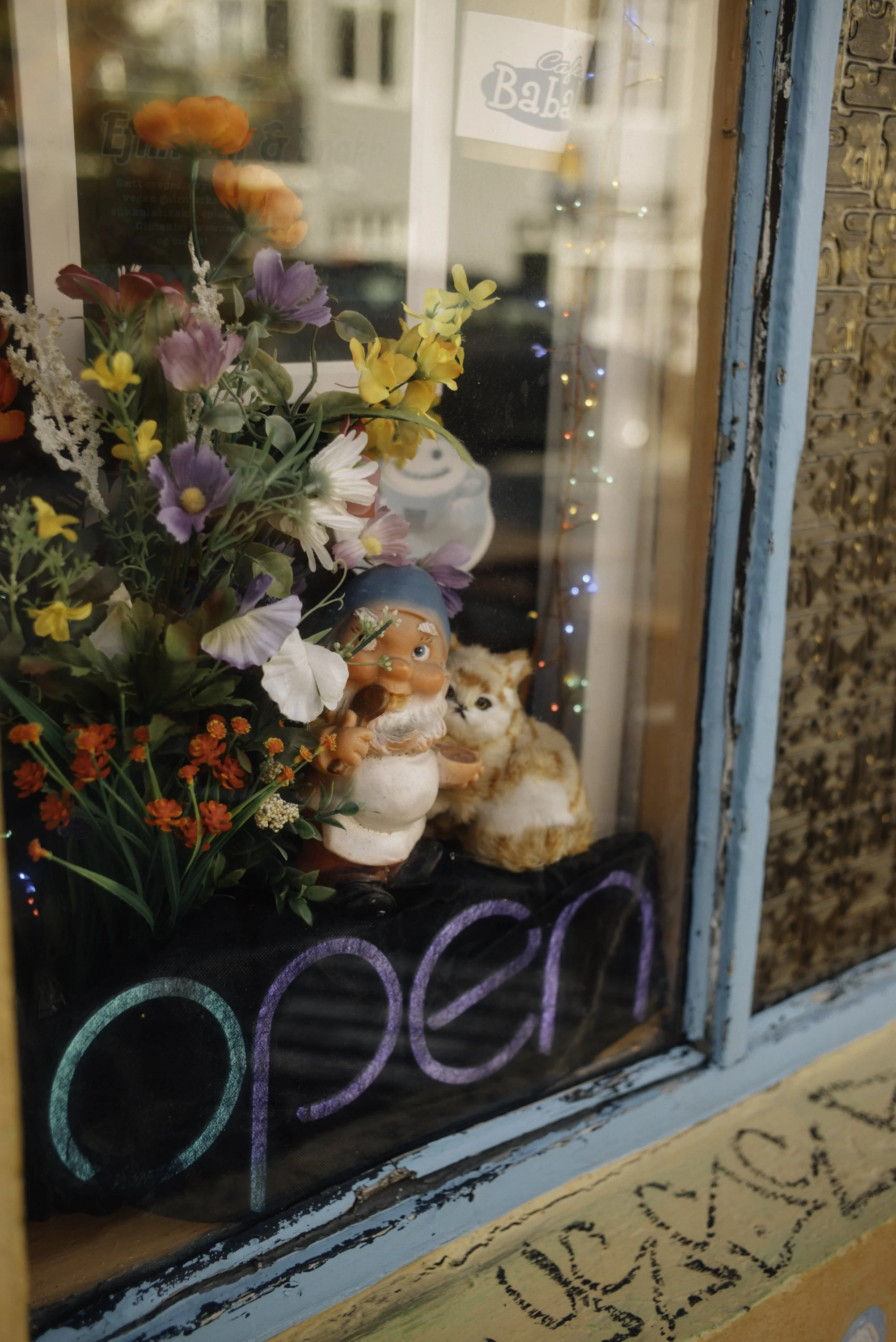 Blumenstrauß, Gartenzwerg und Katzefigur im Schaufenster eines Ladens mit leuchtenden Lichtern.