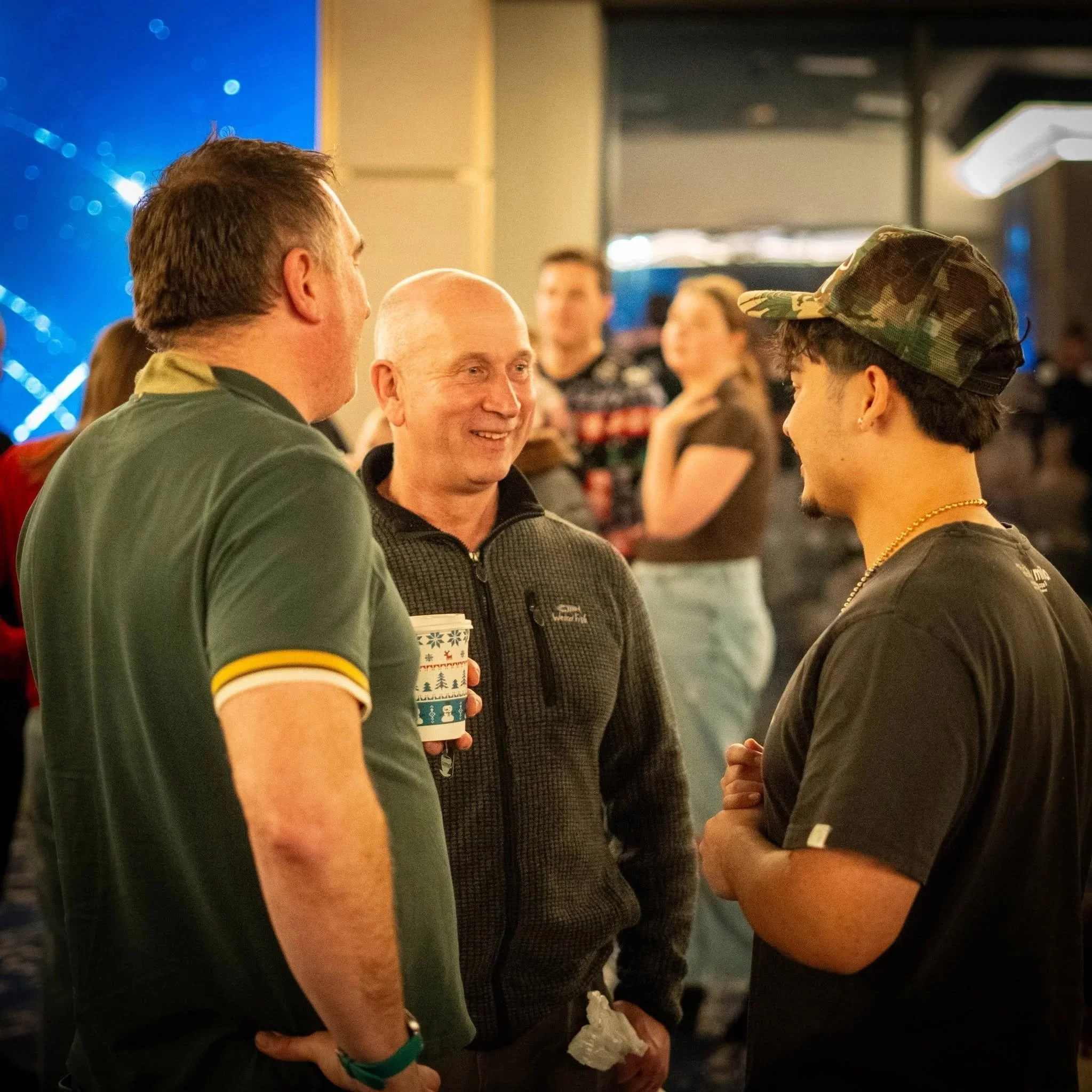 People engaging in conversation at an indoor event, some holding festive cups, in a well-lit space with a lively atmosphere.
