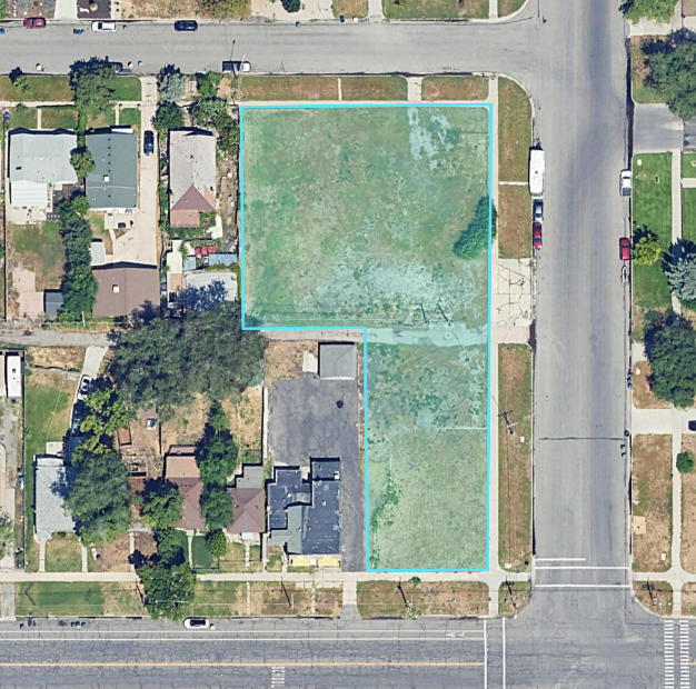 Aerial view of a residential area with a vacant lot outlined in blue, surrounded by houses, trees, and streets.