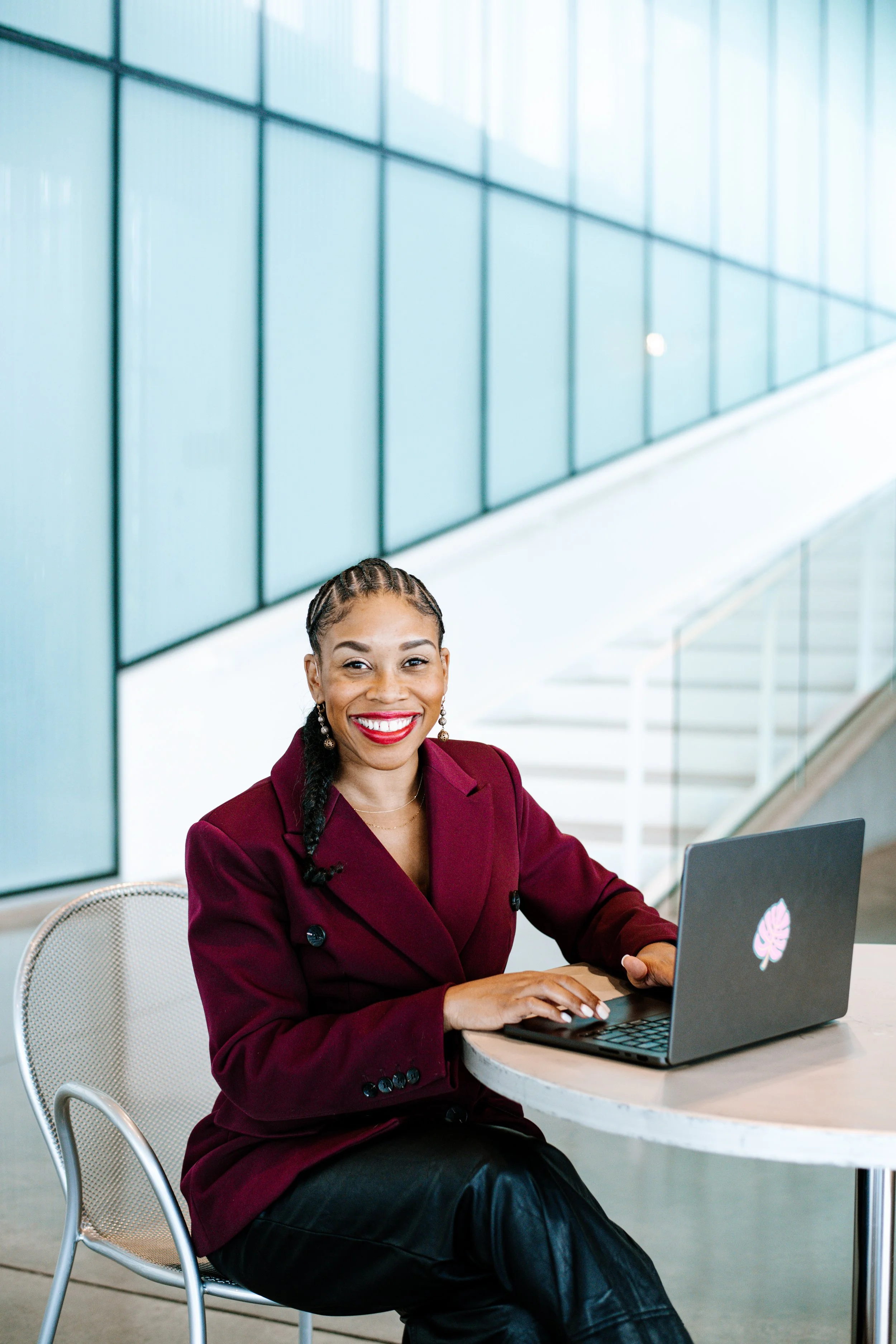 A woman smiling with red lipstick, wearing a yellow blazer with stairs in the background