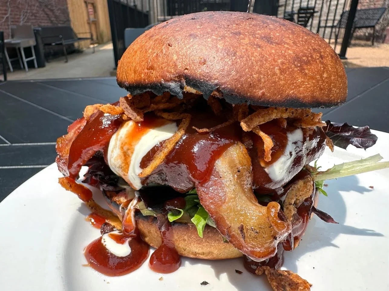 BBQ BURGER: choice of half pound beef or veggie patty with bacon, mixed greens, tomato, fried onion, whipped garlic goat cheese, deep fried garlic mayo and BBQ sauce on a brioche bun, comes with a choice of side.