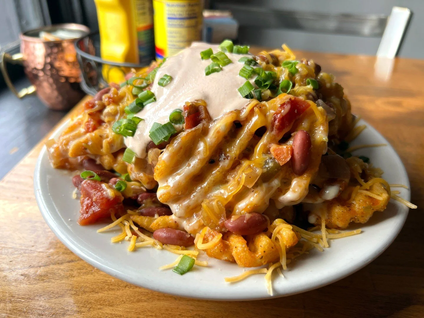 CHILI CHEESE FRIES: waffle fries, vegetarian chili and gouda jalape&ntilde;o cheese sauce, garnished with jalape&ntilde;o-sriracha sour cream and green onions!