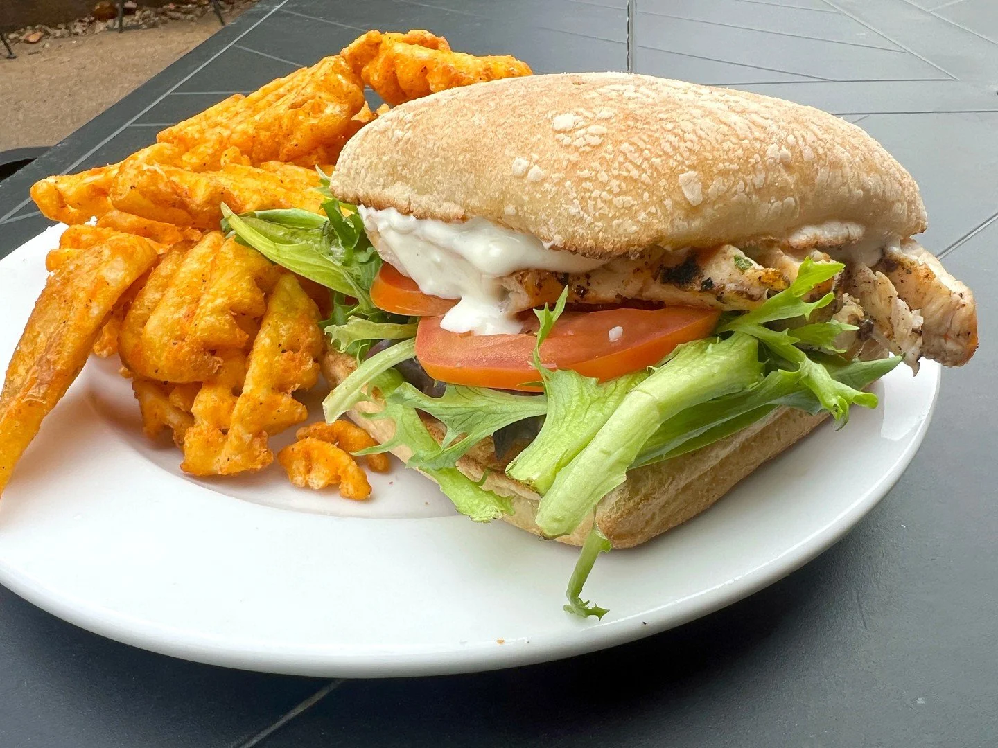 BB's CHICKEN: Grilled chicken breast with mixed greens, tomato, green apple slices, whipped garlic goat cheese, and onion jam on a ciabatta bun, seen here with a side of waffle fries.