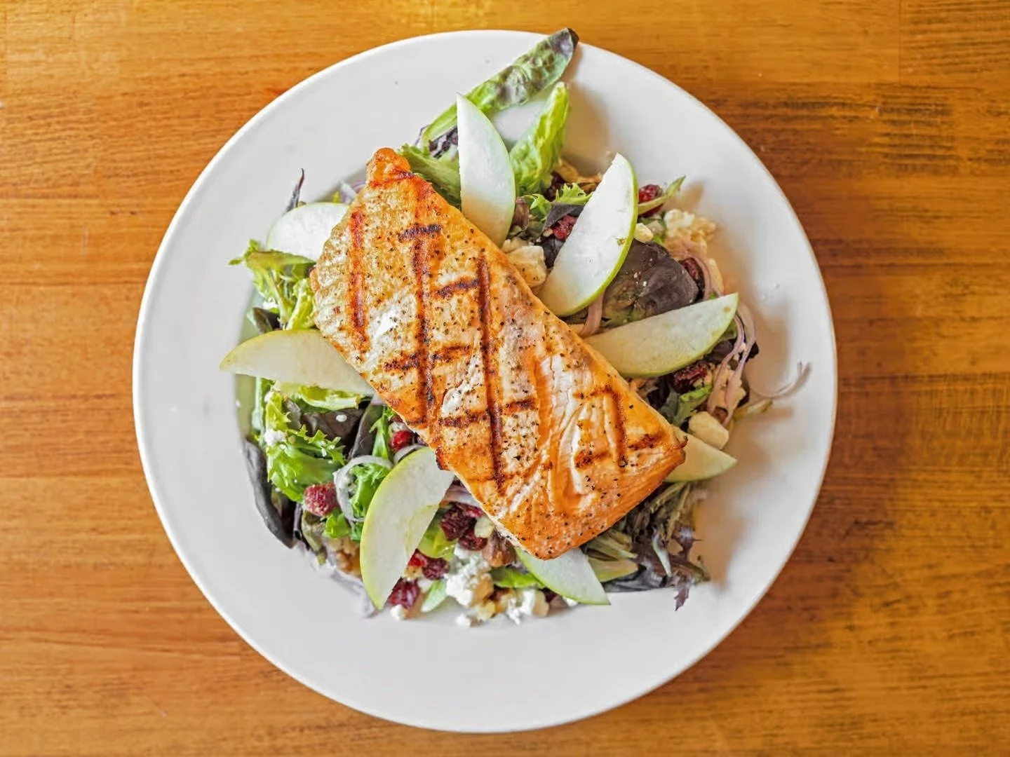 Salmon Salad 🥗: Enjoy a refreshing mix of greens, red onions, crunchy apples, tart cranberries, walnuts, and creamy goat cheese, all drizzled with Jan&rsquo;s balsamic vinaigrette and topped with grilled salmon!