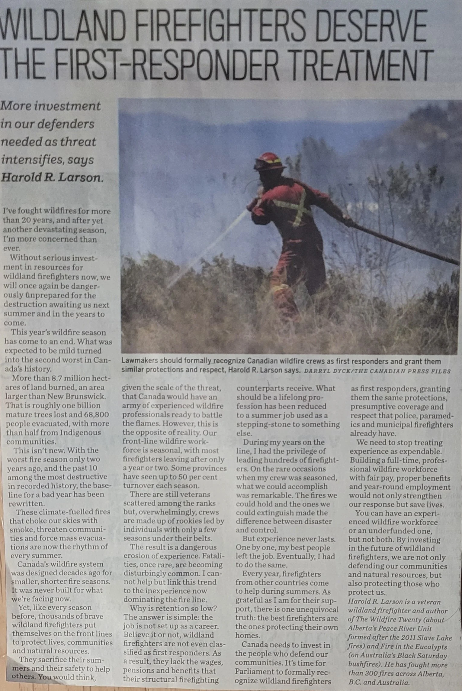 Firefighter in uniform extinguishing a wildfire with a hose amidst smoke and flames, wearing protective gear.
