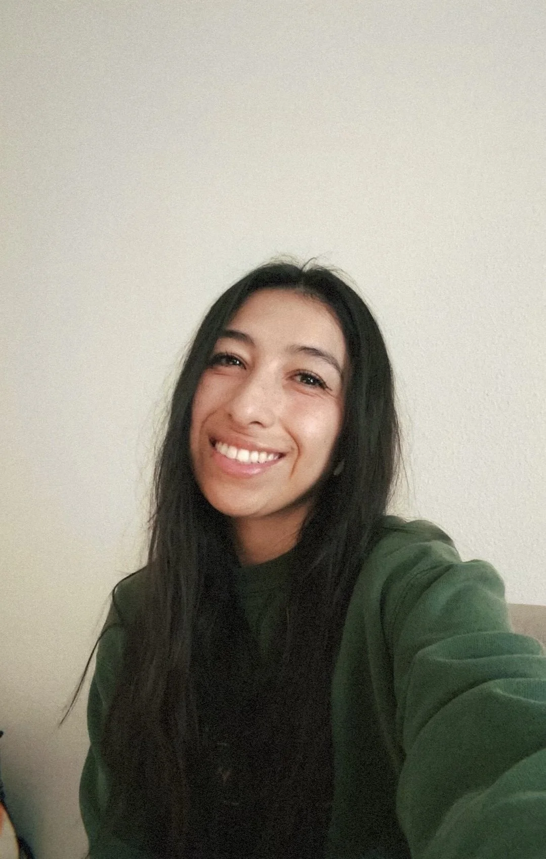 Smiling person with long dark hair wearing a green sweatshirt, timestamp on image.