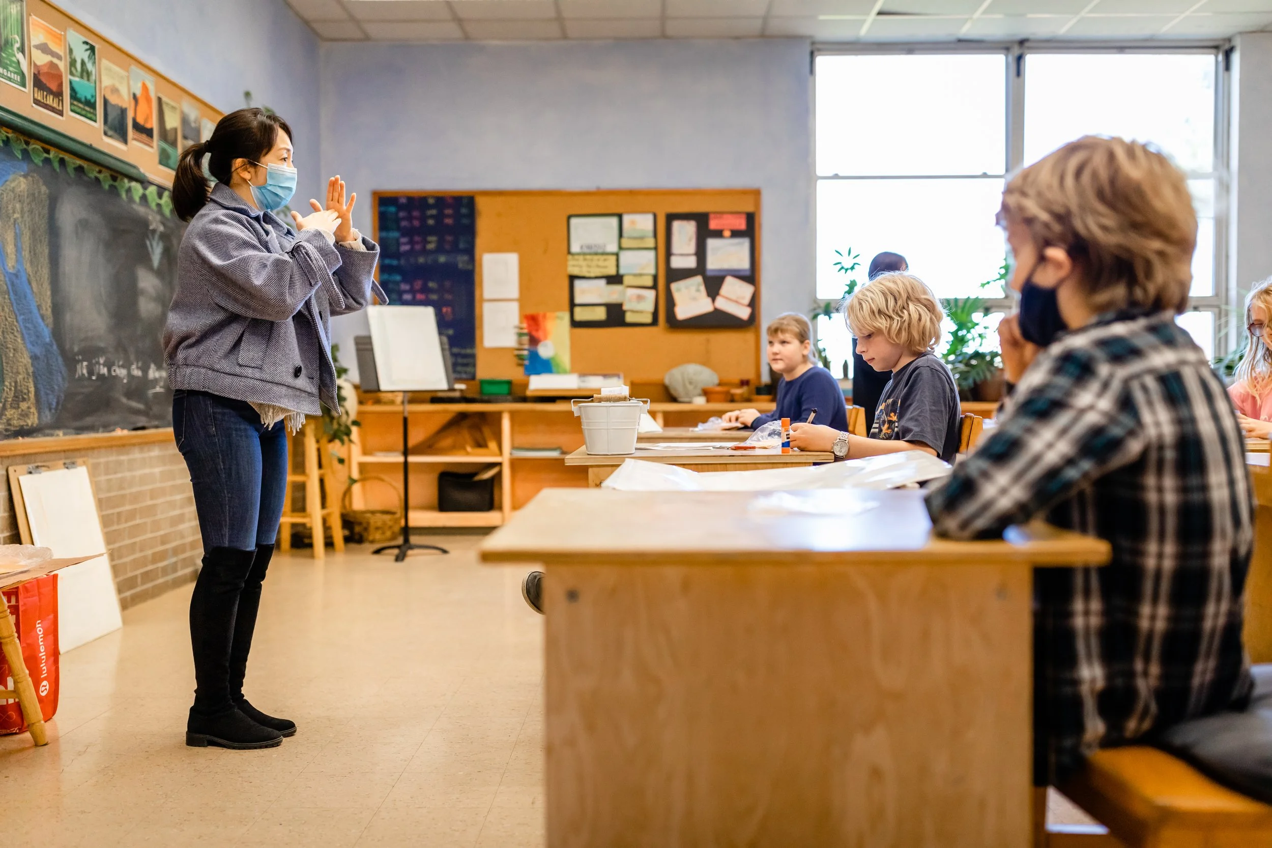 A Mandarin teacher stands in front of a Middle School class of students sitting at desks at the Prairie Moon Waldorf School in Lawrence Kansas. The students are looking at the teacher who is gesturing with her hands as she works in a foreign language