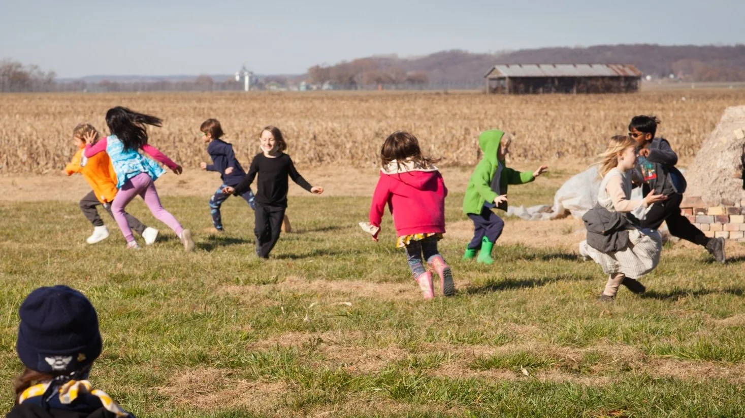 Children running outdoors in a field playing a game of tag with joyful faces. Wearing bring colors as they play with friends in a speciality class outside.