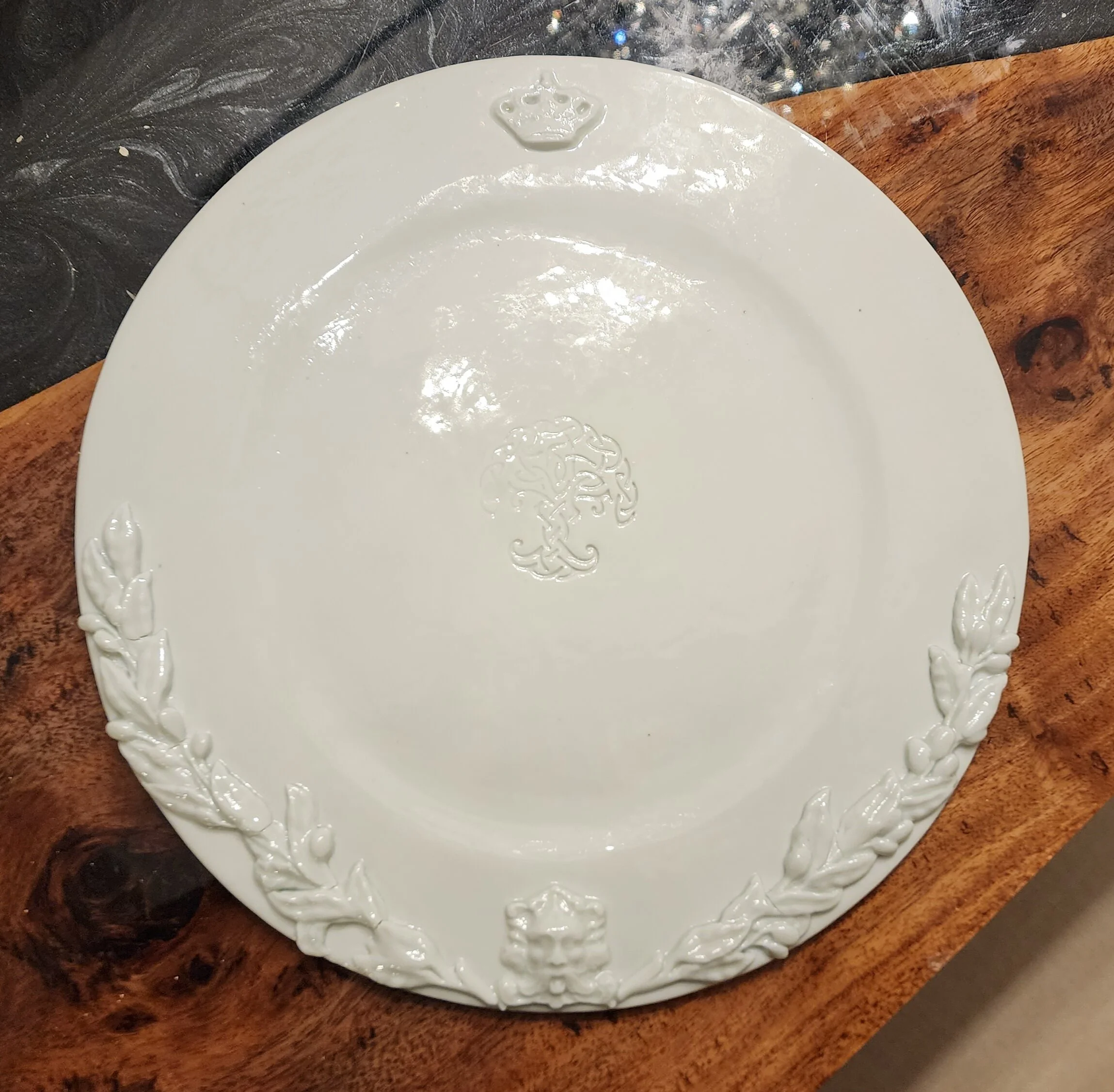 White ceramic plate with embossed crown and decorative floral embossing on the rim, placed on a wooden surface. Porcelain, Irish heritage.
