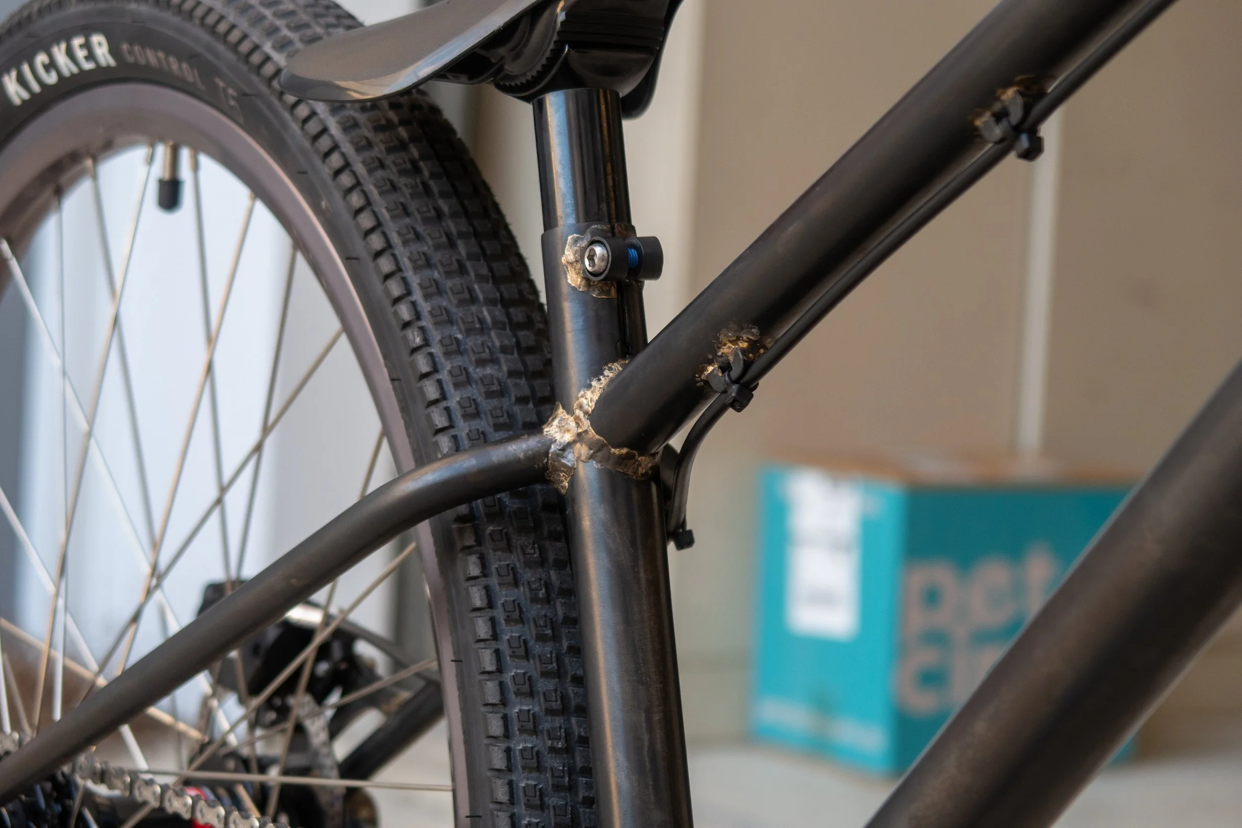 Close-up of the rear part of an electric bicycle, showing the rear wheel with a knobby tire, part of the frame, and the rear suspension mechanism.