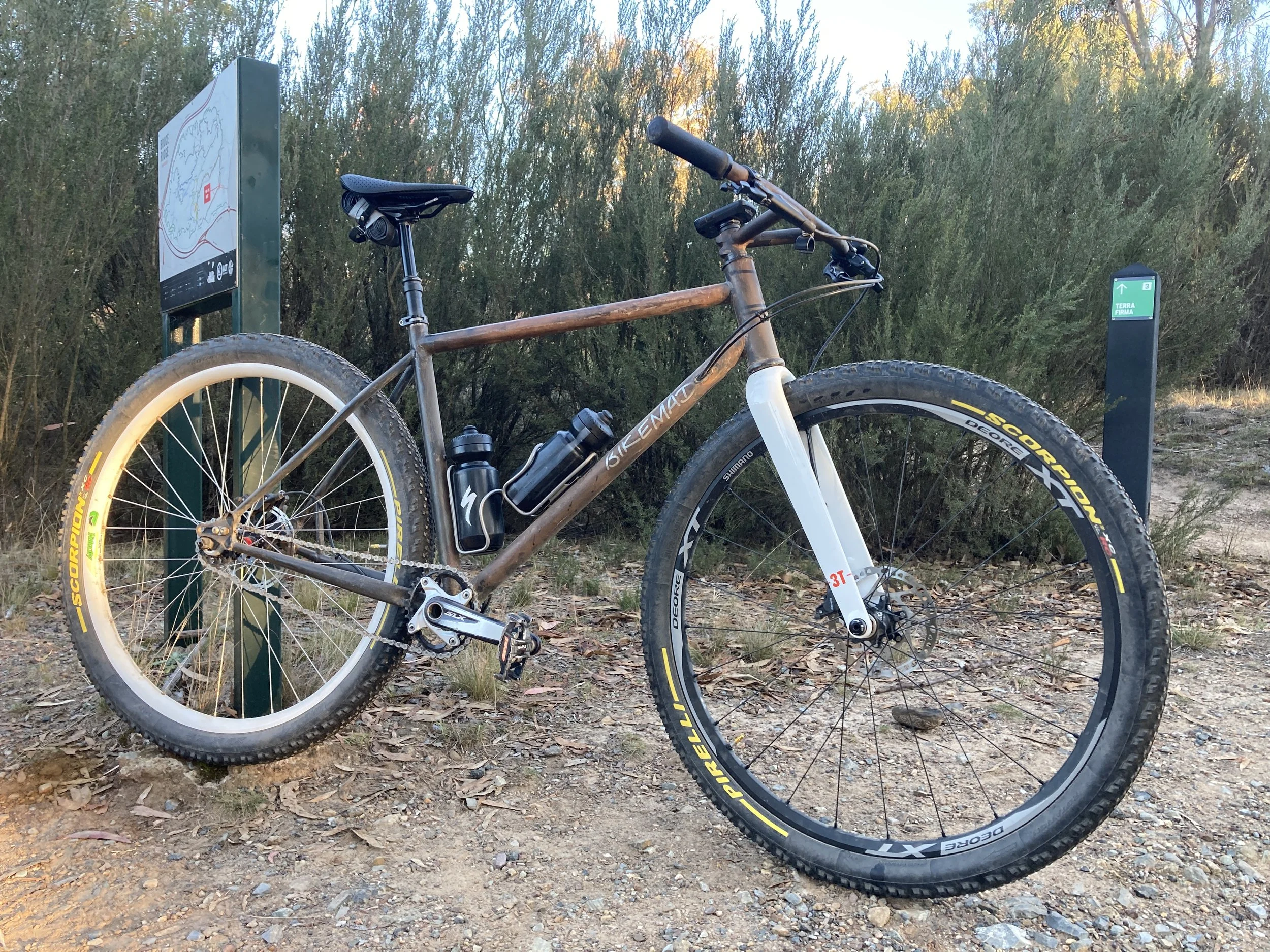 A mountain bike parked by a trail sign in a natural outdoor setting.