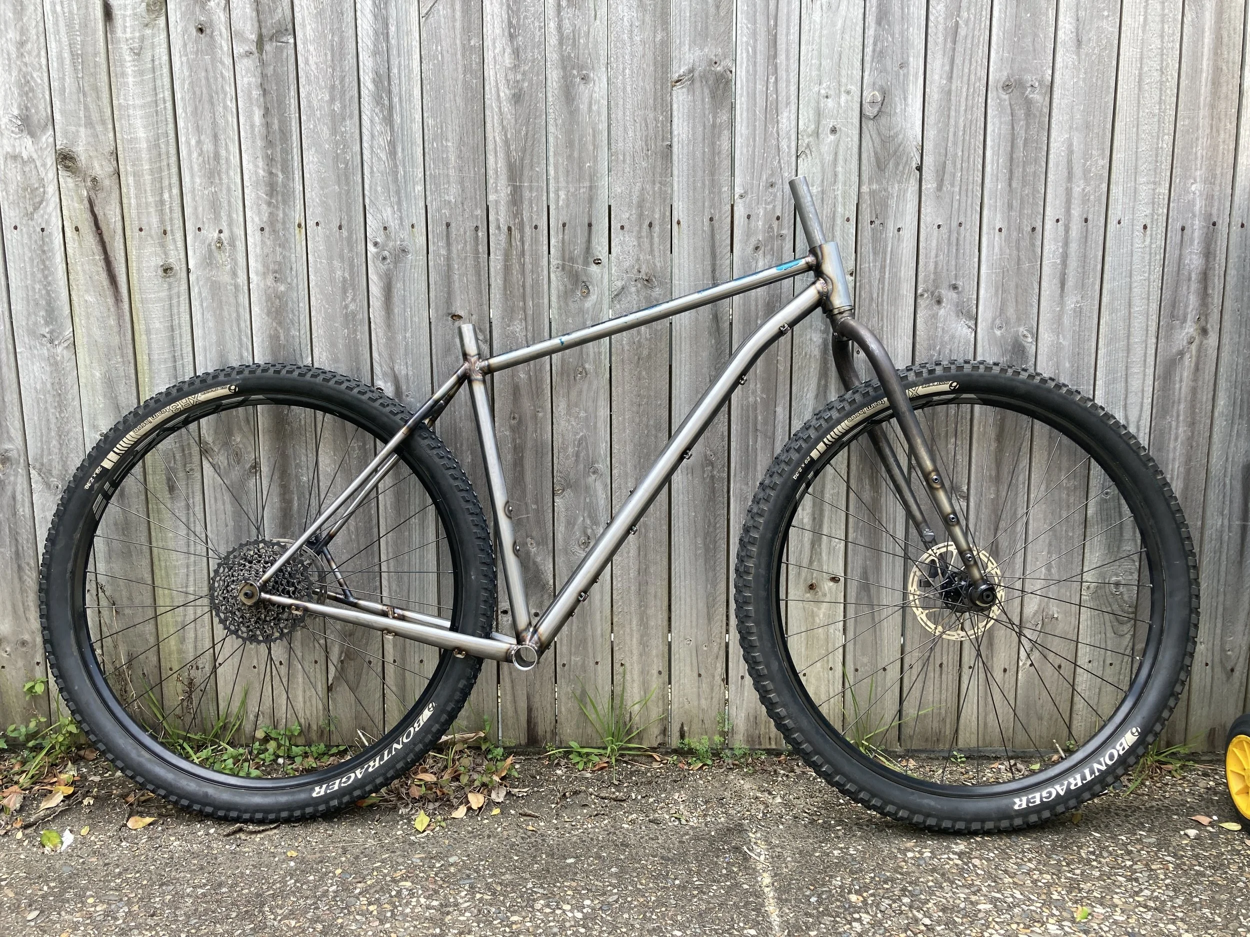 A bicycle with a metallic frame and wide tires, leaning against a wooden fence.