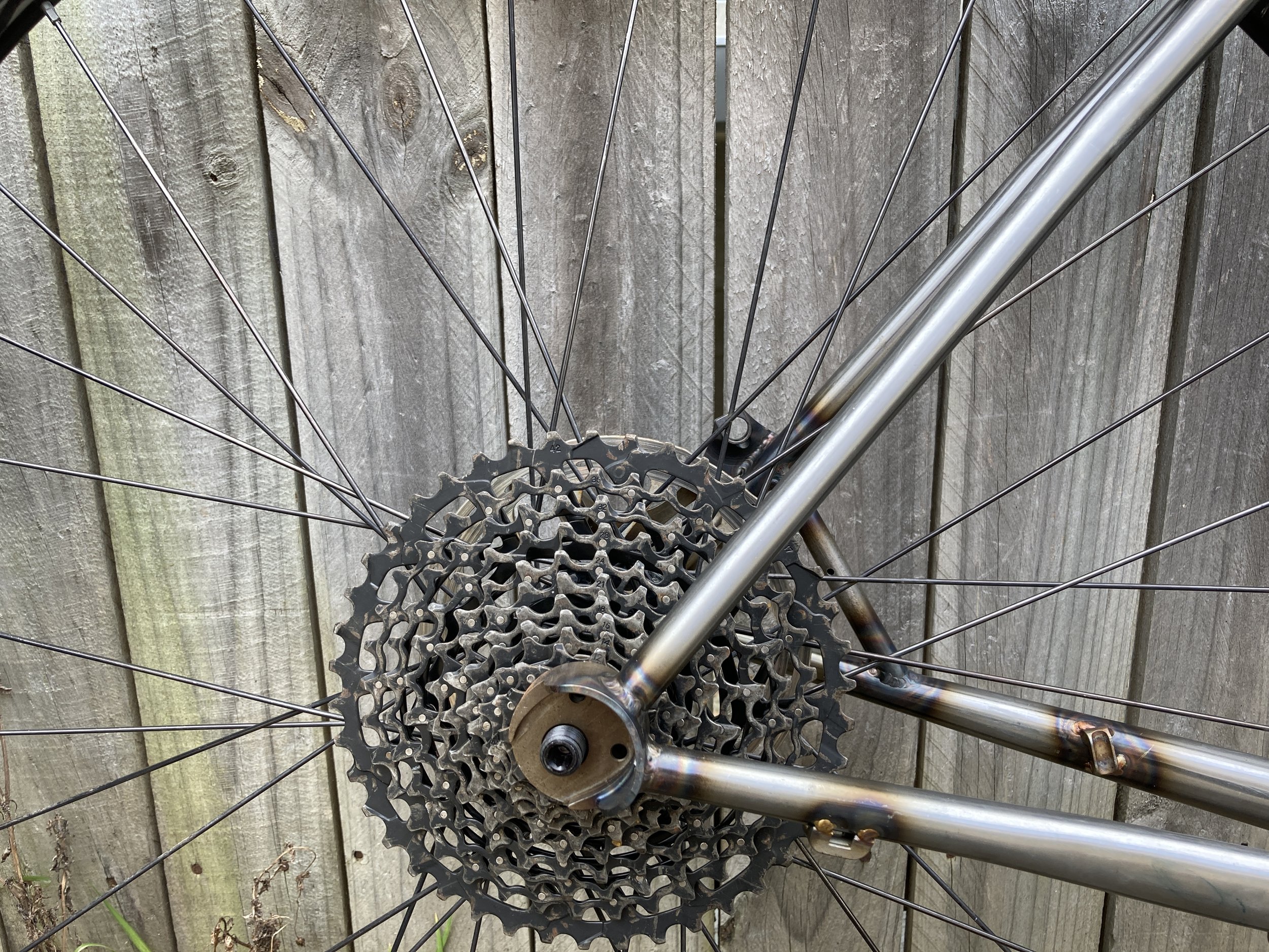 Close-up of a bicycle's rear wheel, cassette, and part of the frame against a wooden fence.
