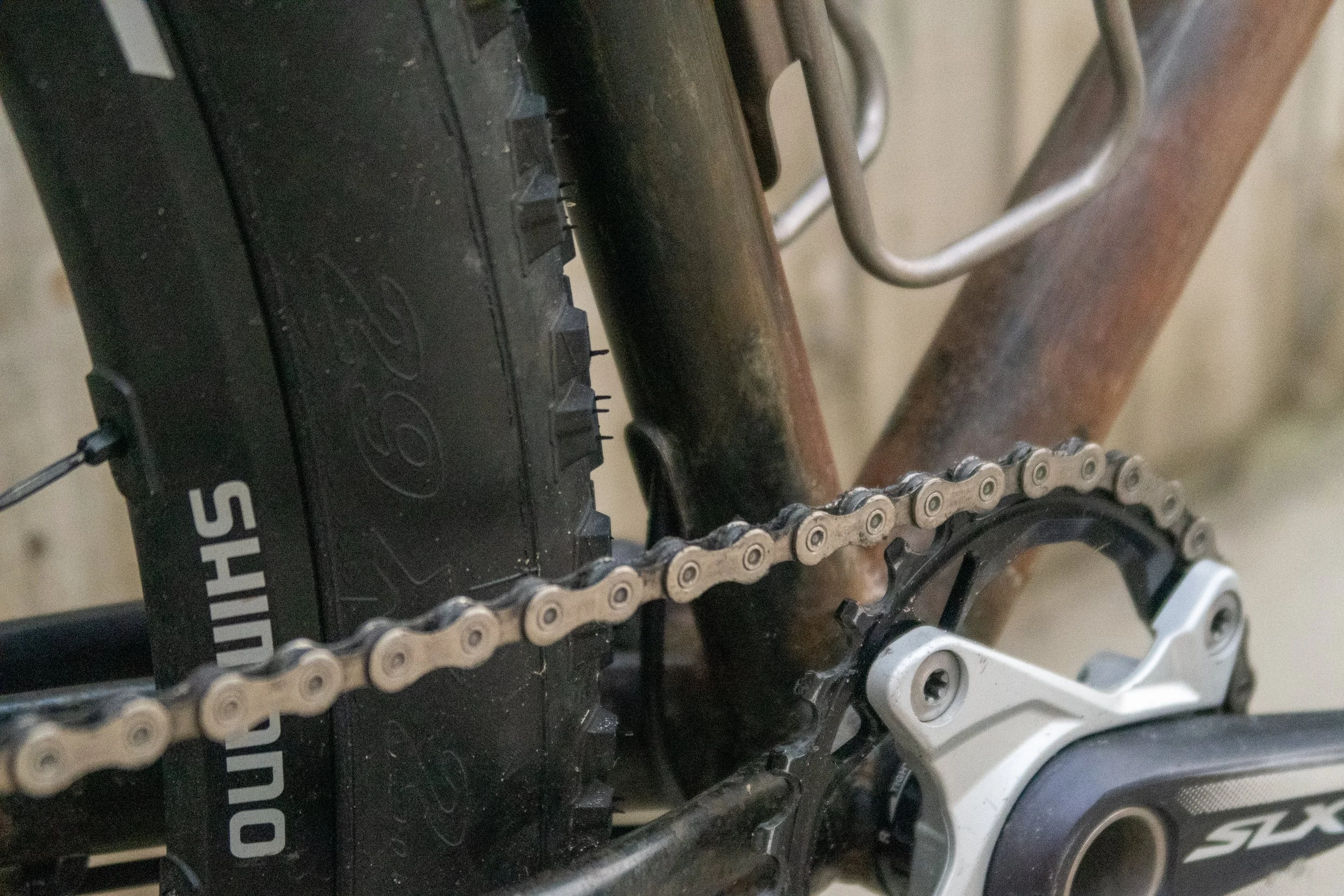 Close-up of a mountain bike's chain, gear, and part of the frame, with visible rust on the frame and a worn tire.