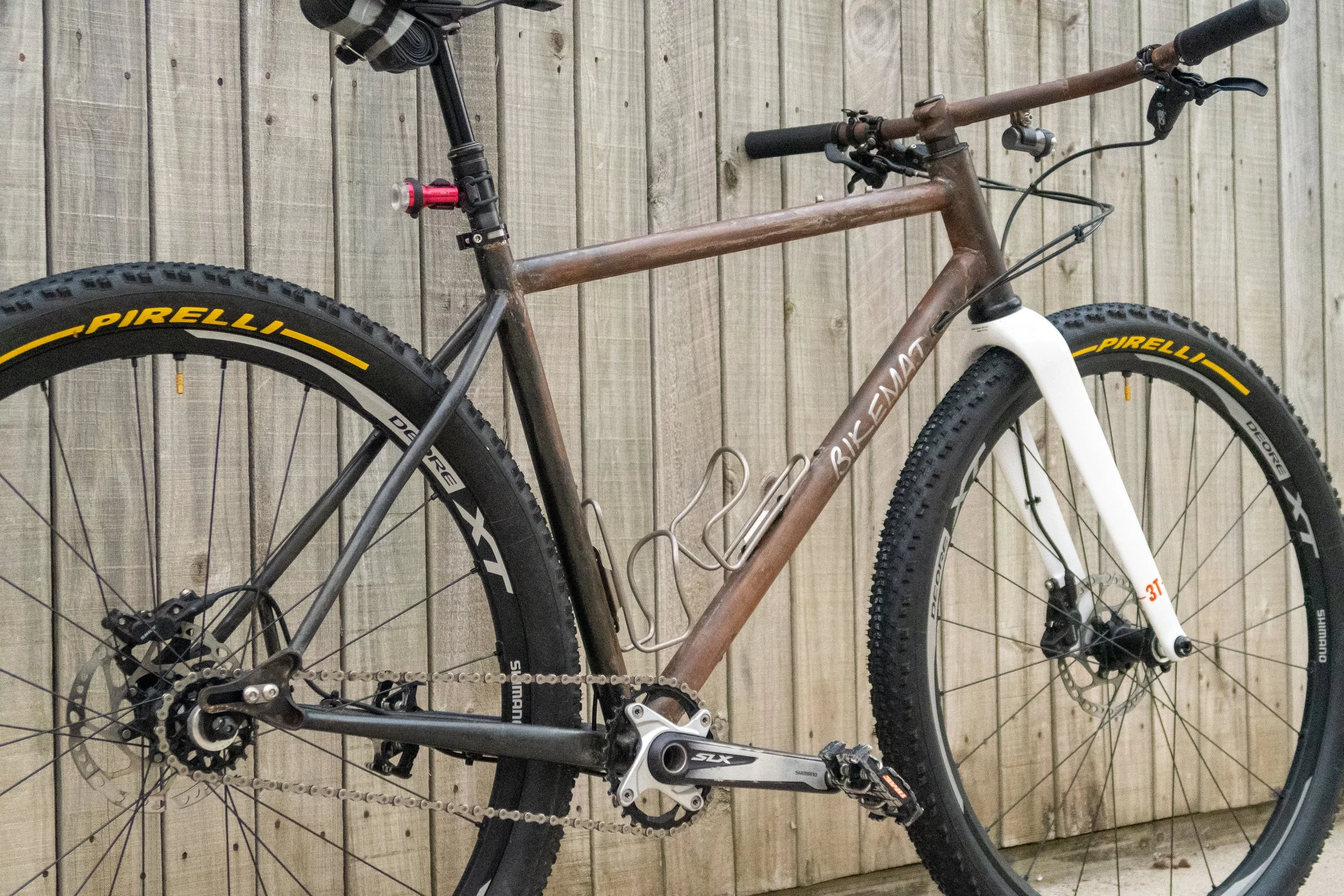 A mountain bike with a brown frame, white front fork, and black and yellow Pirelli tires, leaning against a wooden fence.