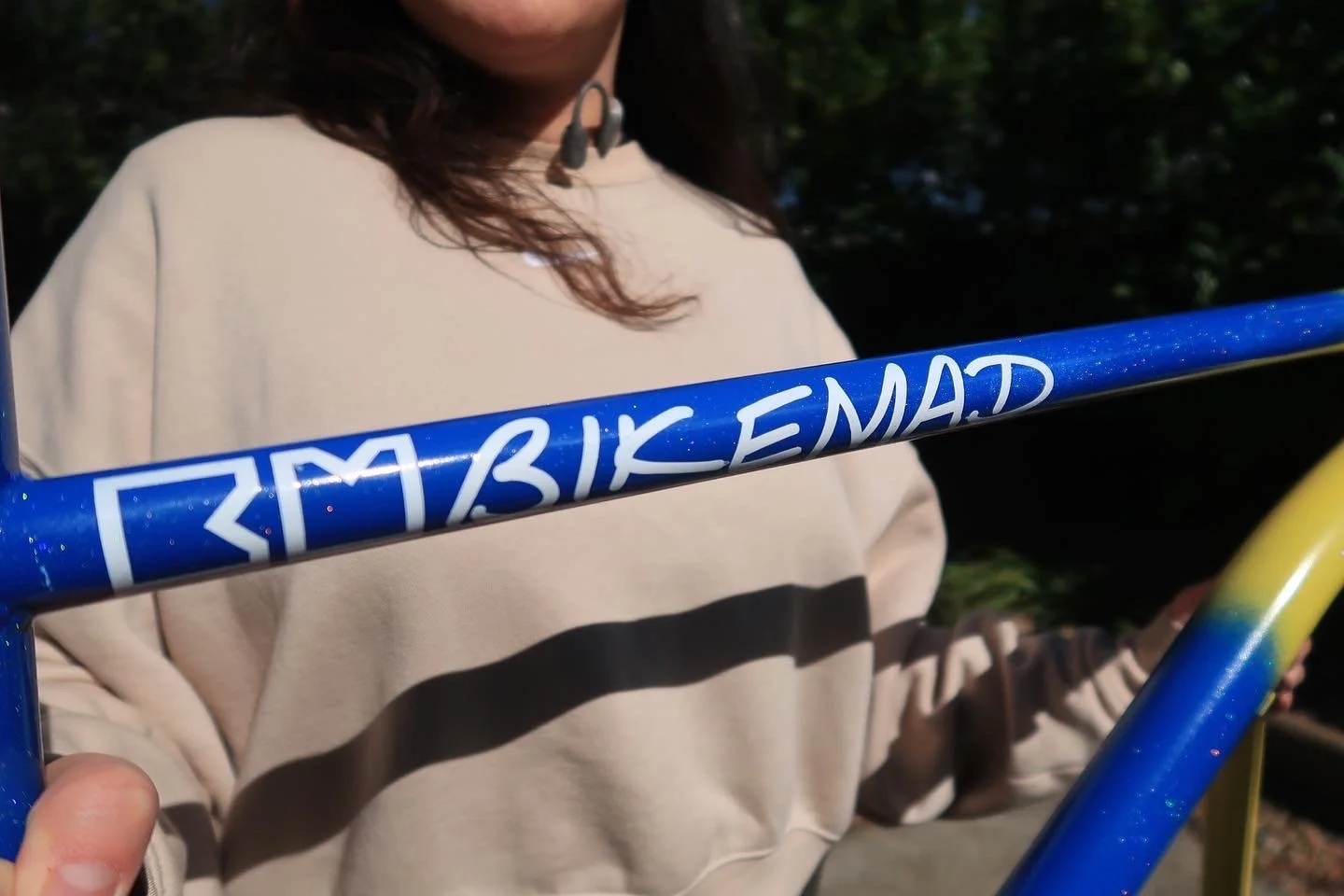 A woman holding a colorful bicycle at night, with part of the bicycle frame and handlebars visible. The frame is blue with white writing, and the handlebars are yellow.
