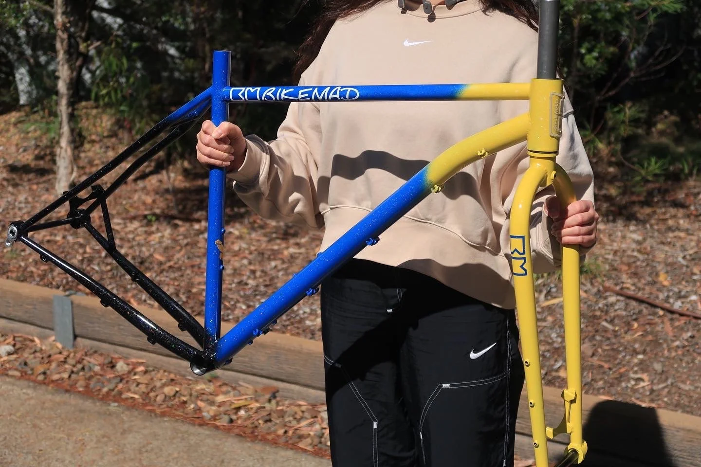 Person holding a yellow and blue bicycle frame outdoors.