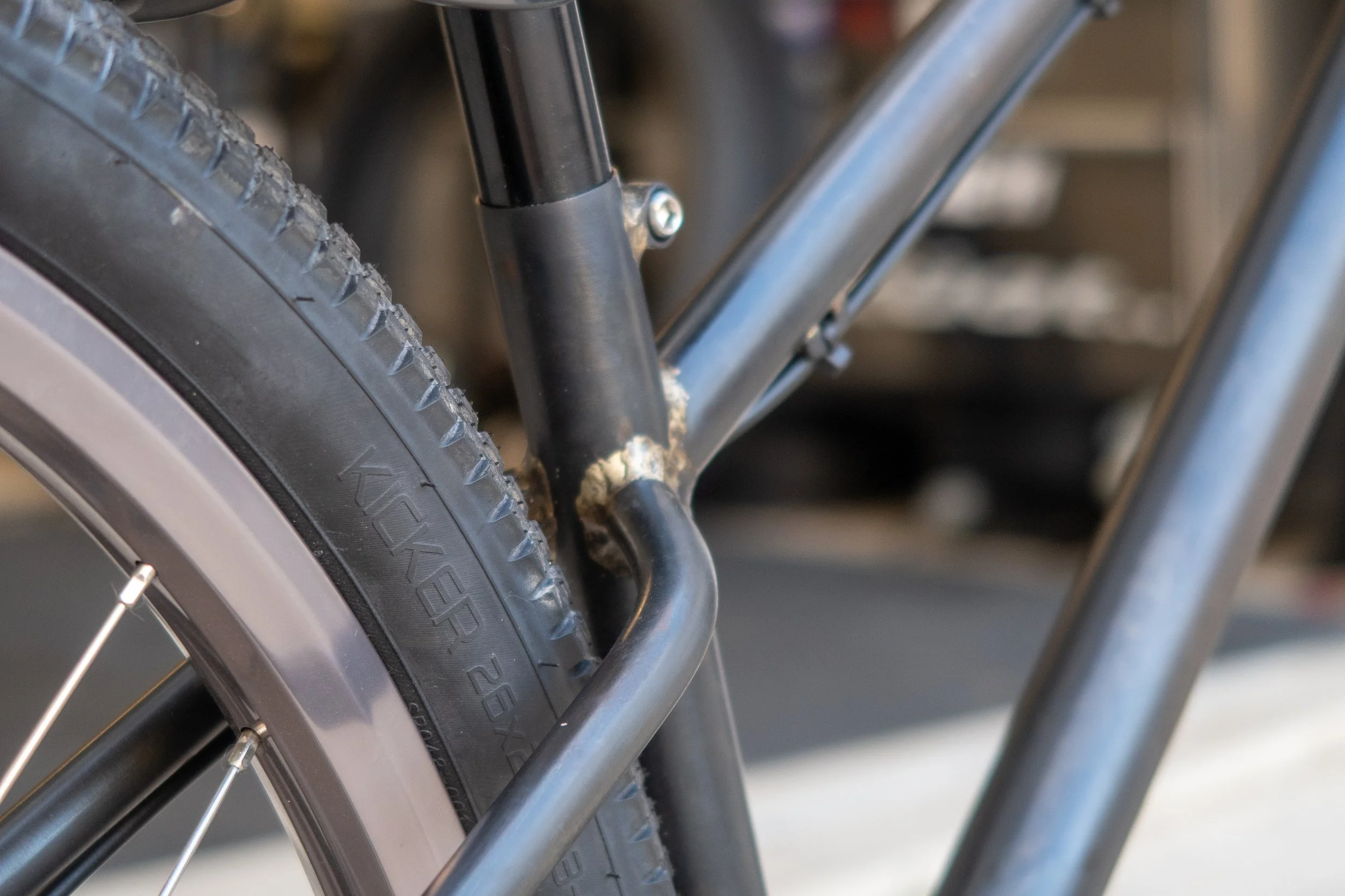 Close-up of a bicycle wheel and frame, showing the tire, metal frame, and part of the rear wheel and derailleur.