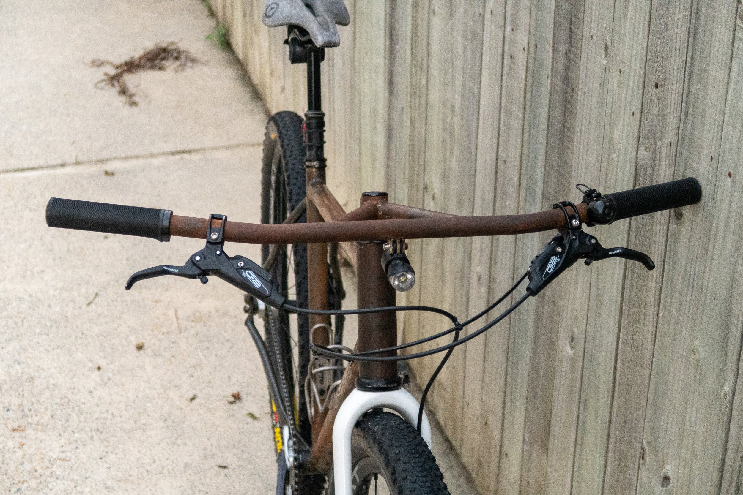 A mountain bike leaning against a wooden fence on a concrete sidewalk.