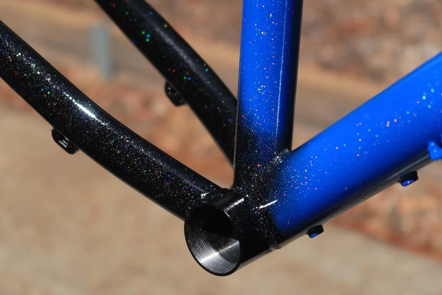 Close-up of a bicycle frame with black and blue glittery paint, showing the head tube and part of the top and down tubes.