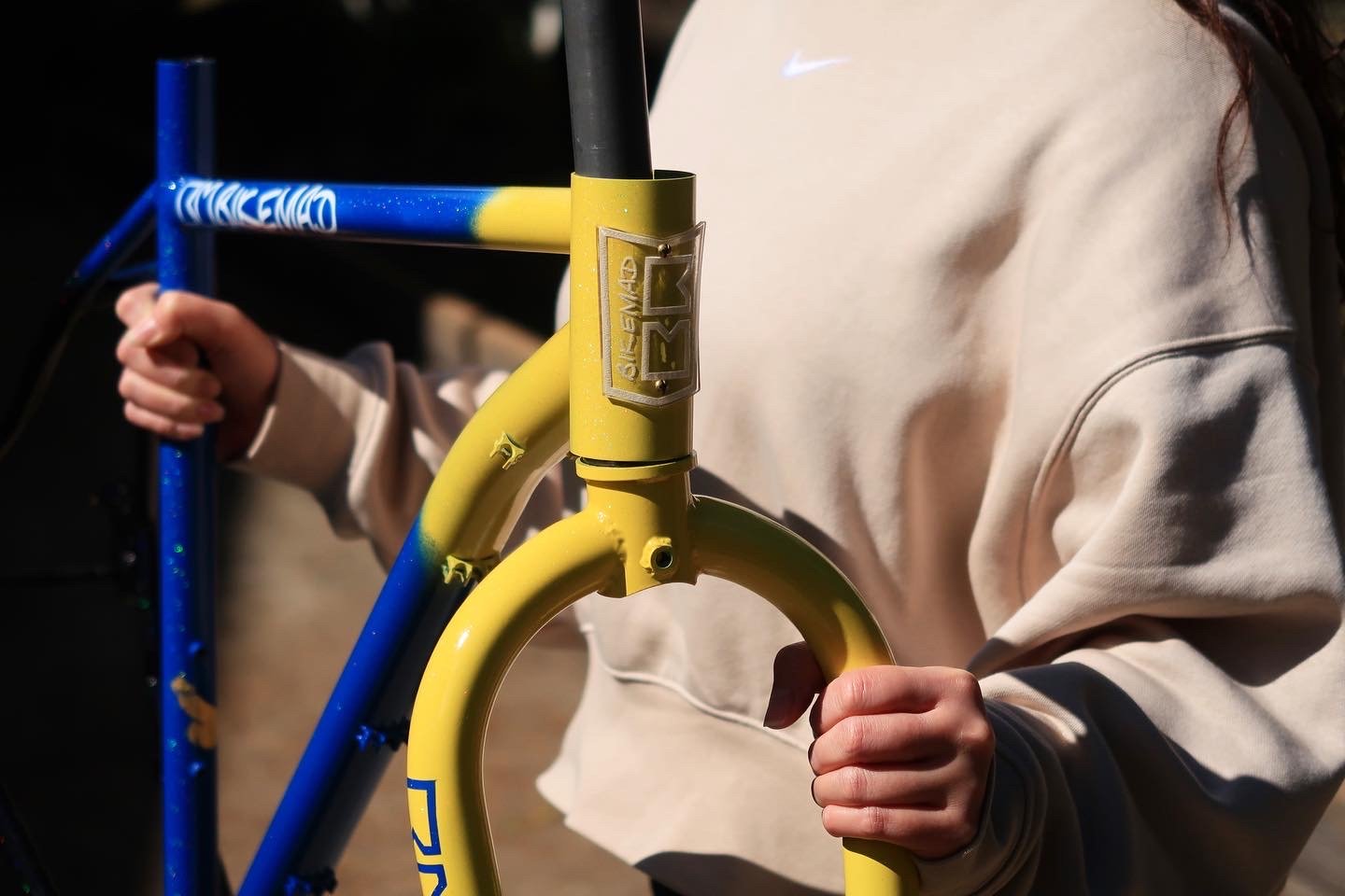 Person holding a yellow and blue BMX bicycle frame.