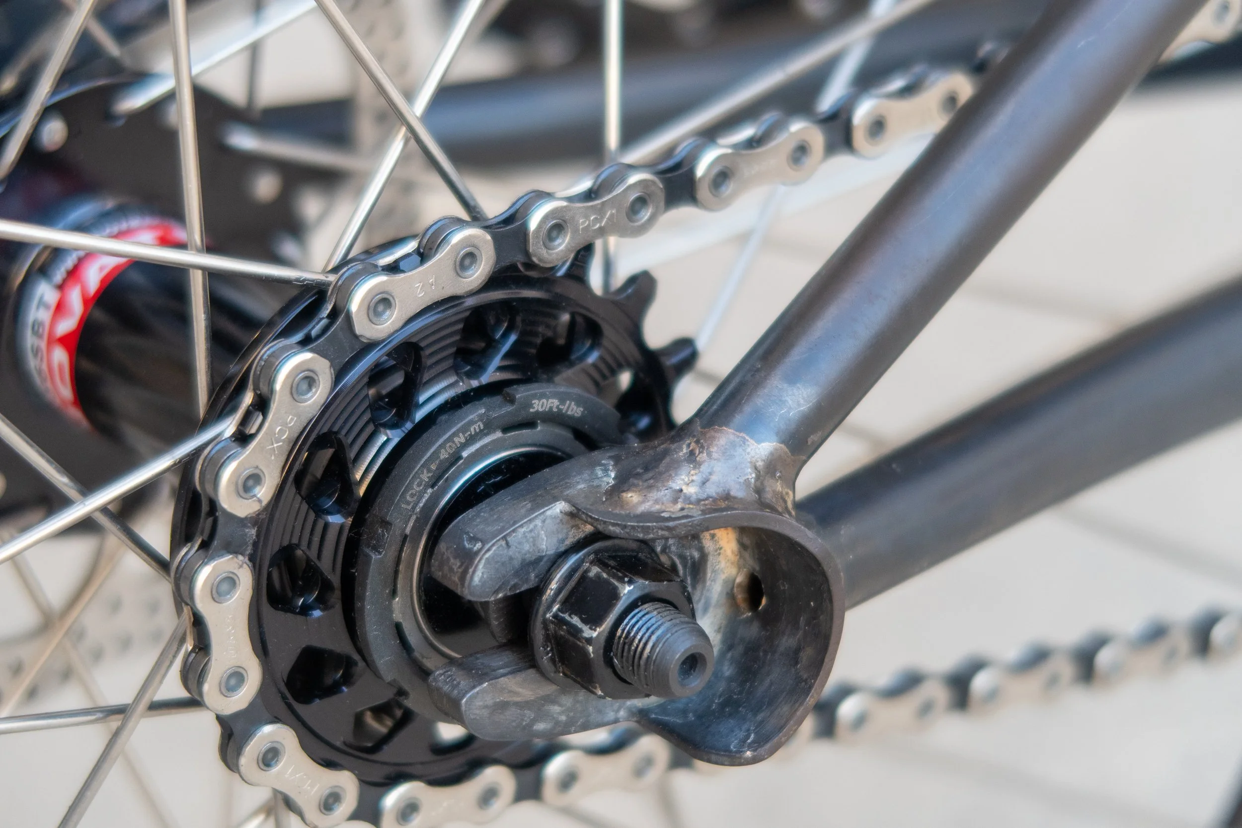Close-up of a bicycle's rear wheel hub, gear, and chain, with visible metal spokes and frame.