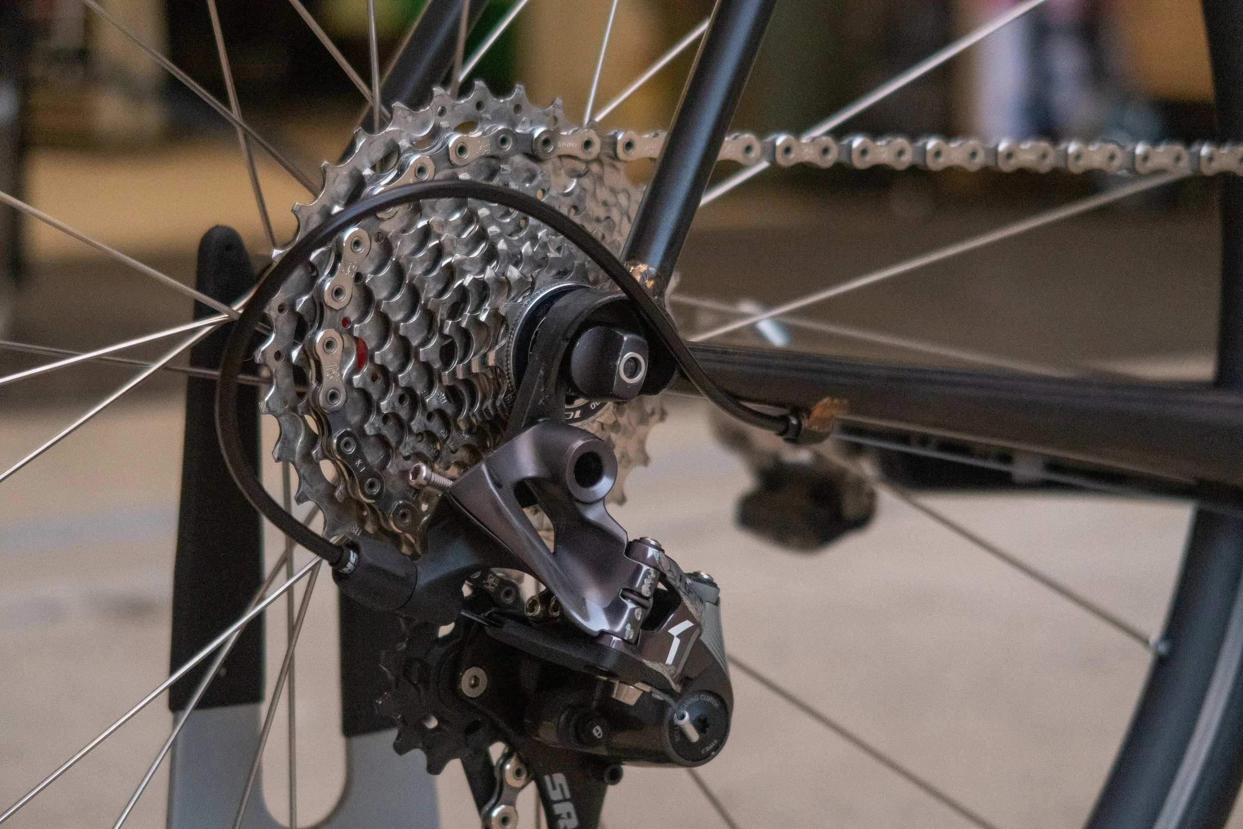 Close-up of the rear derailleur and gear cassette of a road bicycle, with the chain on the gears and part of the black frame visible.