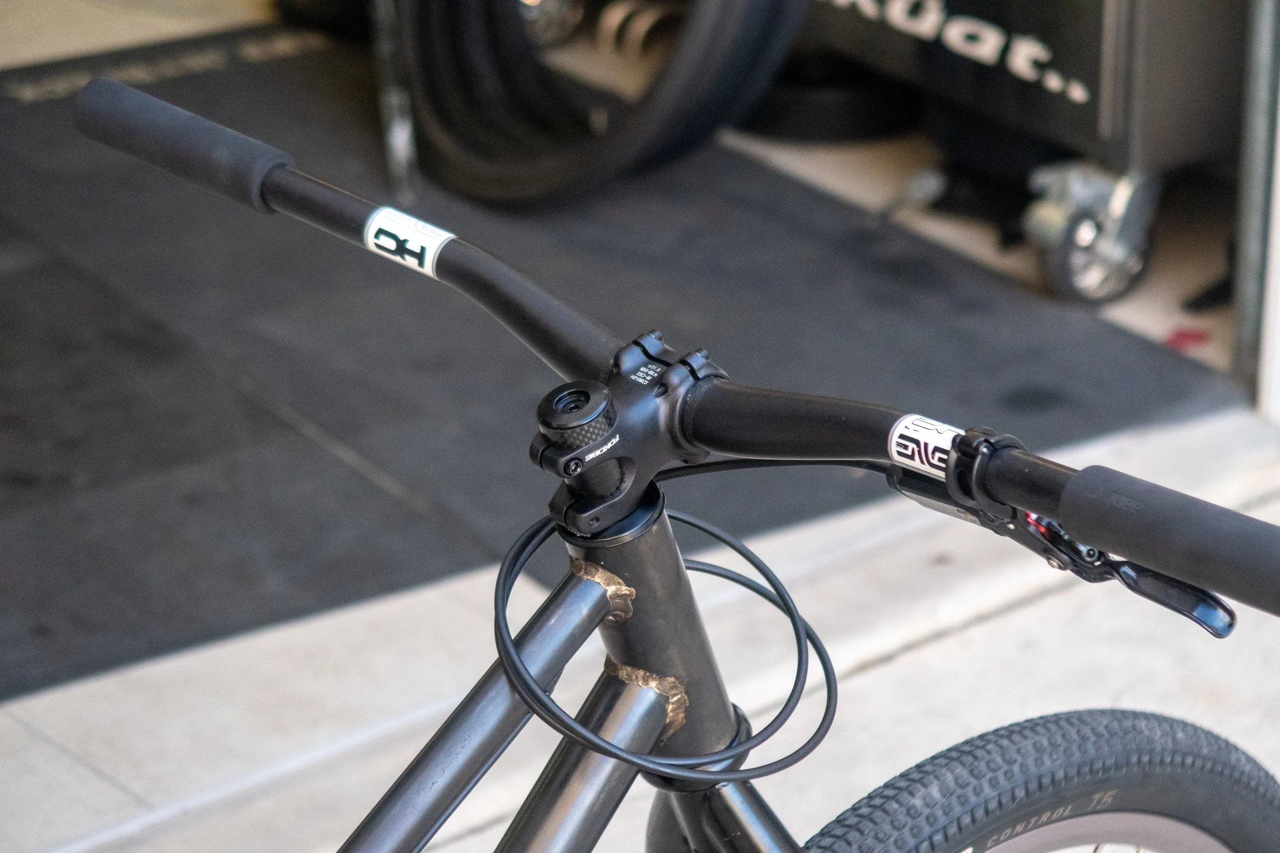 Close-up of a mountain bike handlebar and front tire, with a workshop or garage background.
