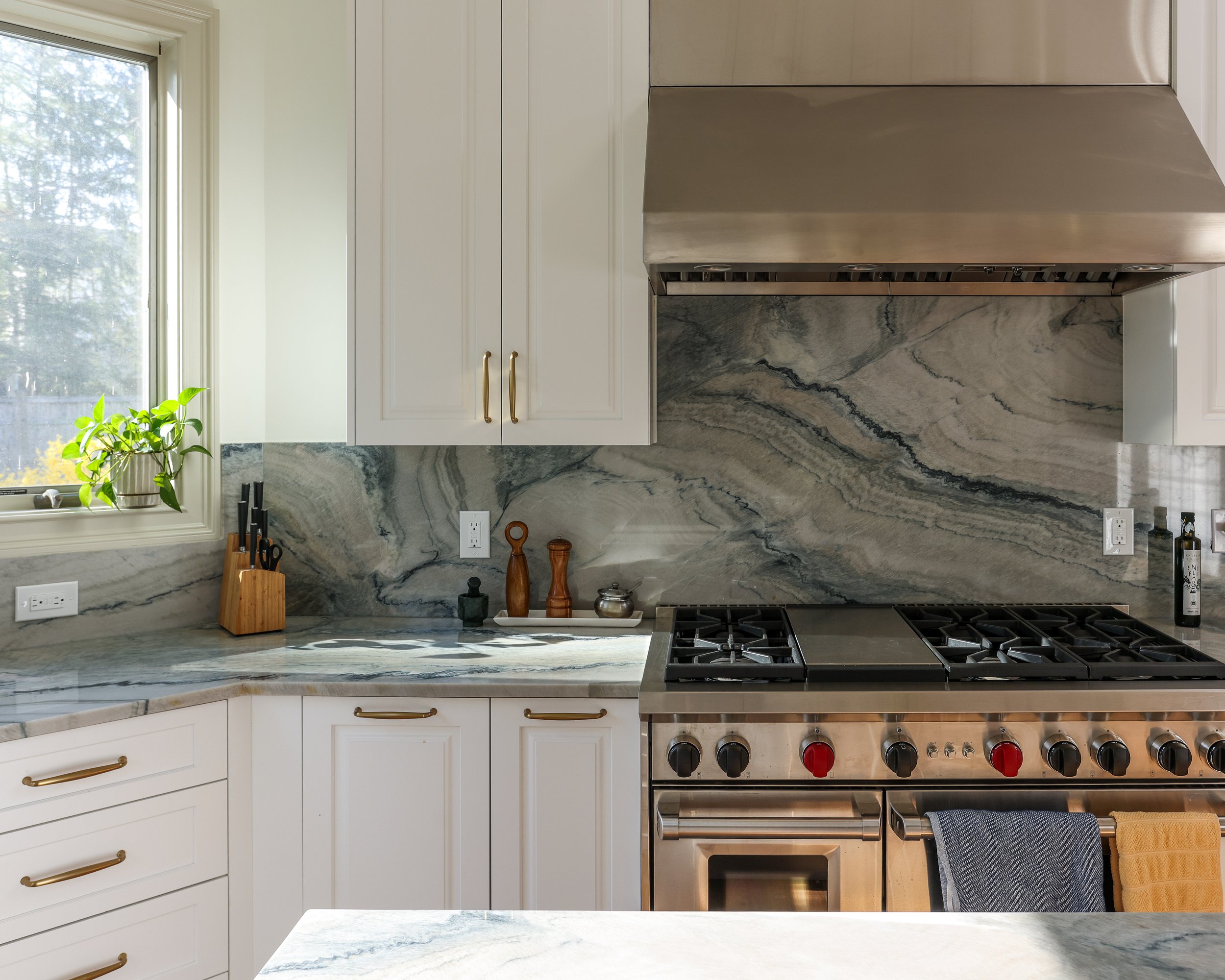 stainless stove and hood surrounded by white cabinets and a grey stone countertop and backsplash