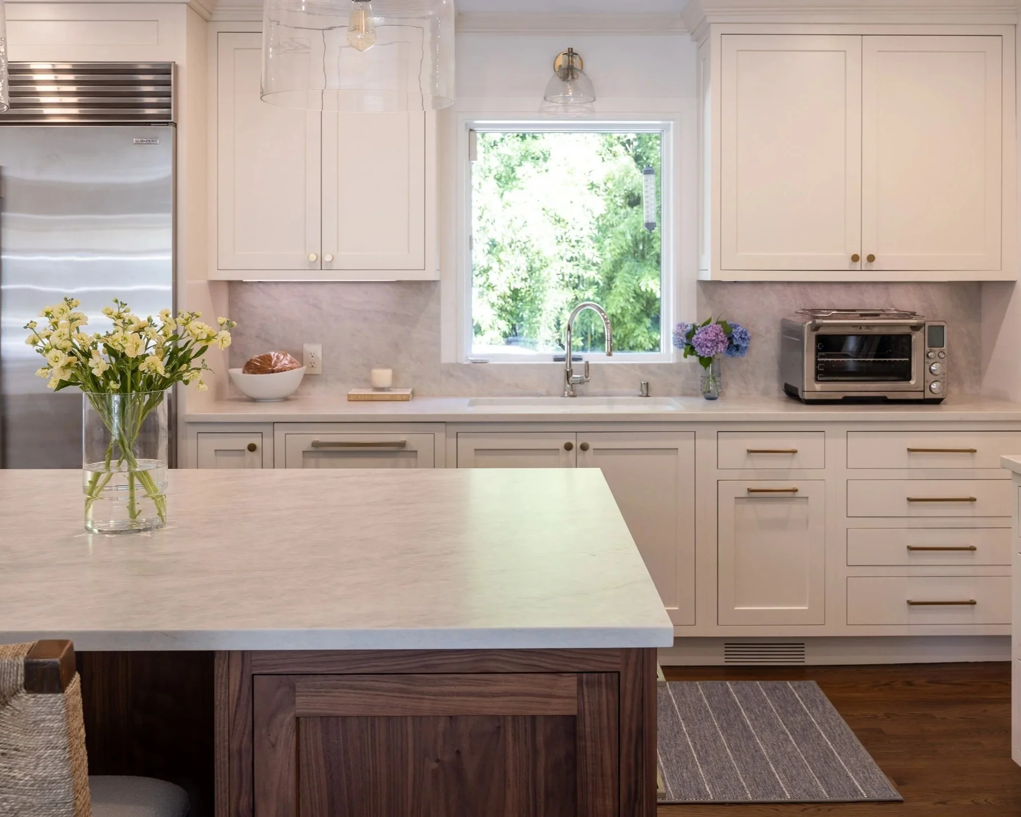a kitchen with a window over a sink, white cabinets and white/light gray counterotps and backsplash
