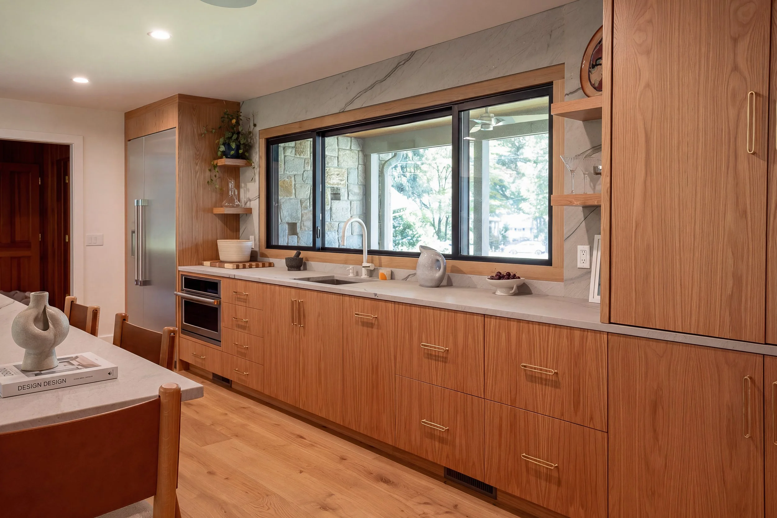 an area of a kitchen with wooden cabinets, a sink, a large window and stainless appliances